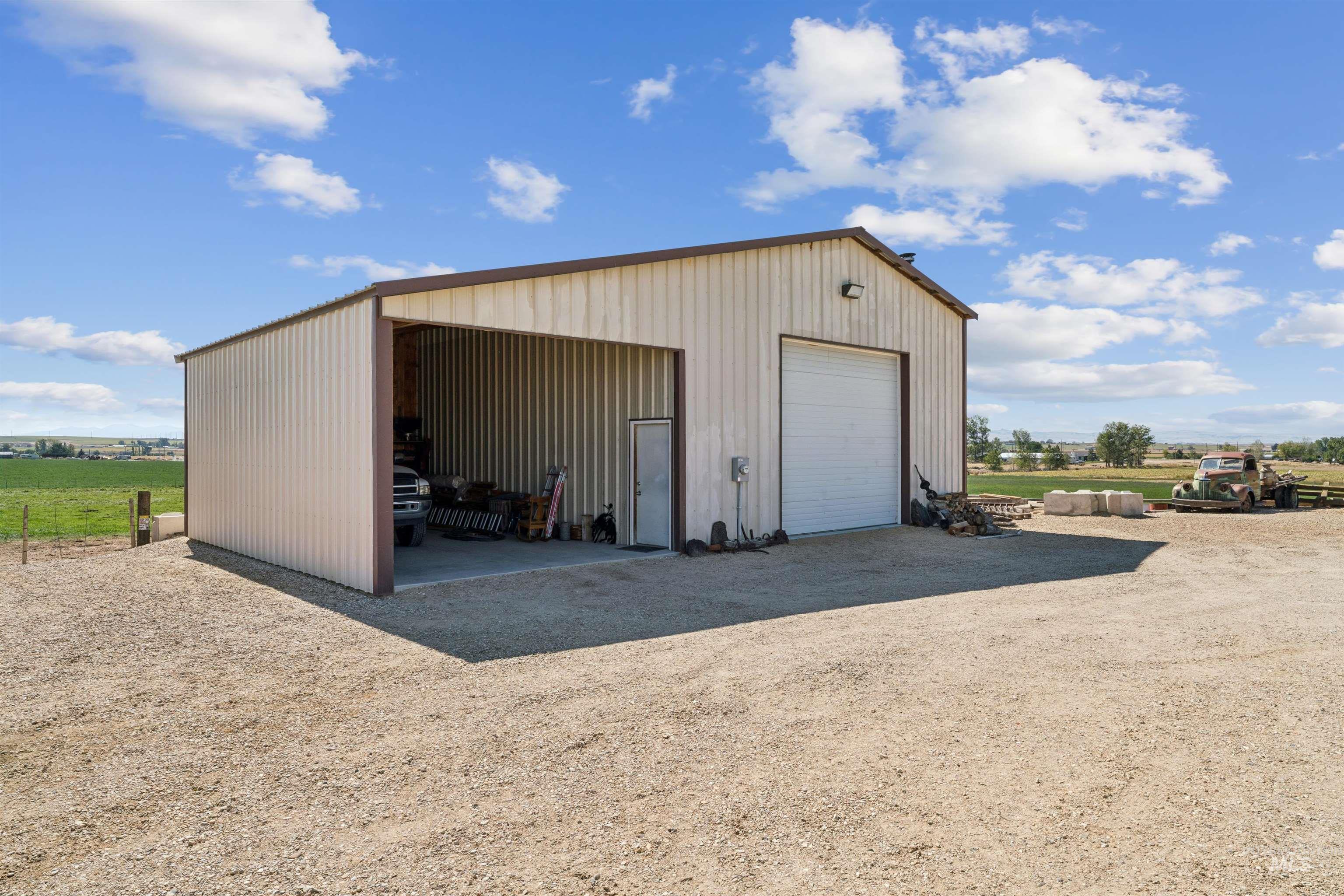 Metal workshop with an open equipment bay and roll-up garage door beside a gravel yard.
