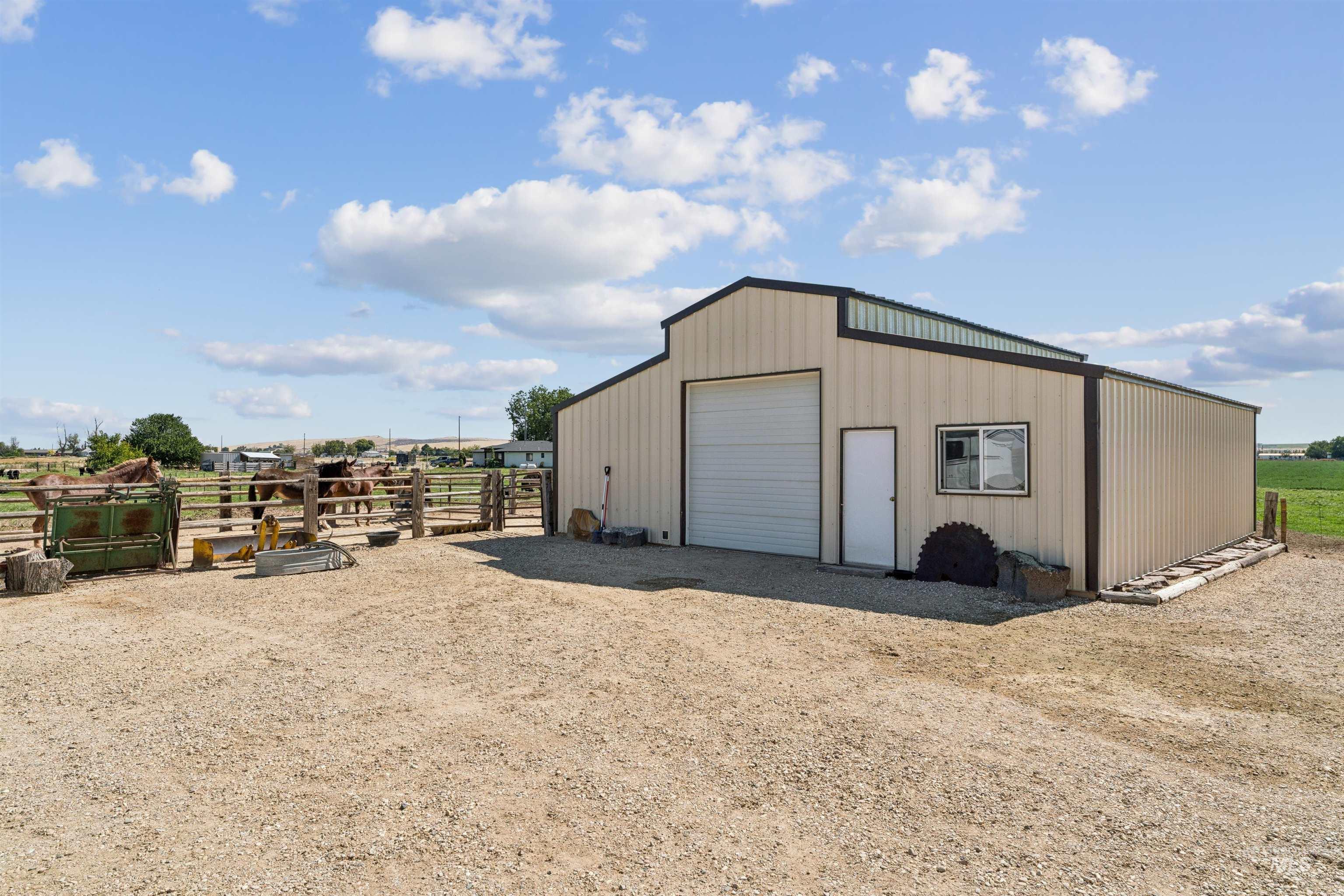 Beige metal barn with a large garage door beside a fenced paddock of horses.