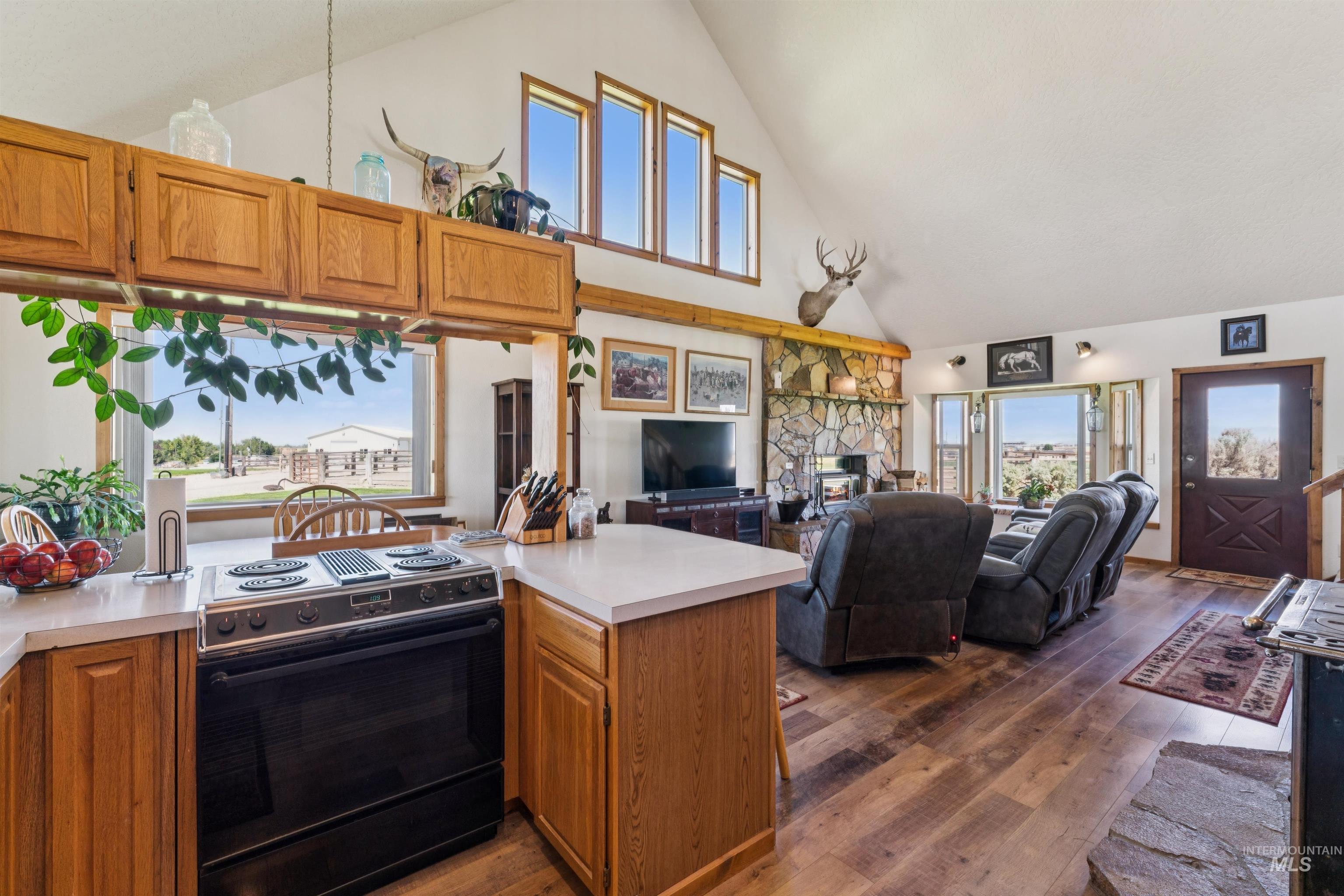 Open-plan kitchen and living room with wood cabinetry, vaulted ceiling, and a stone fireplace.