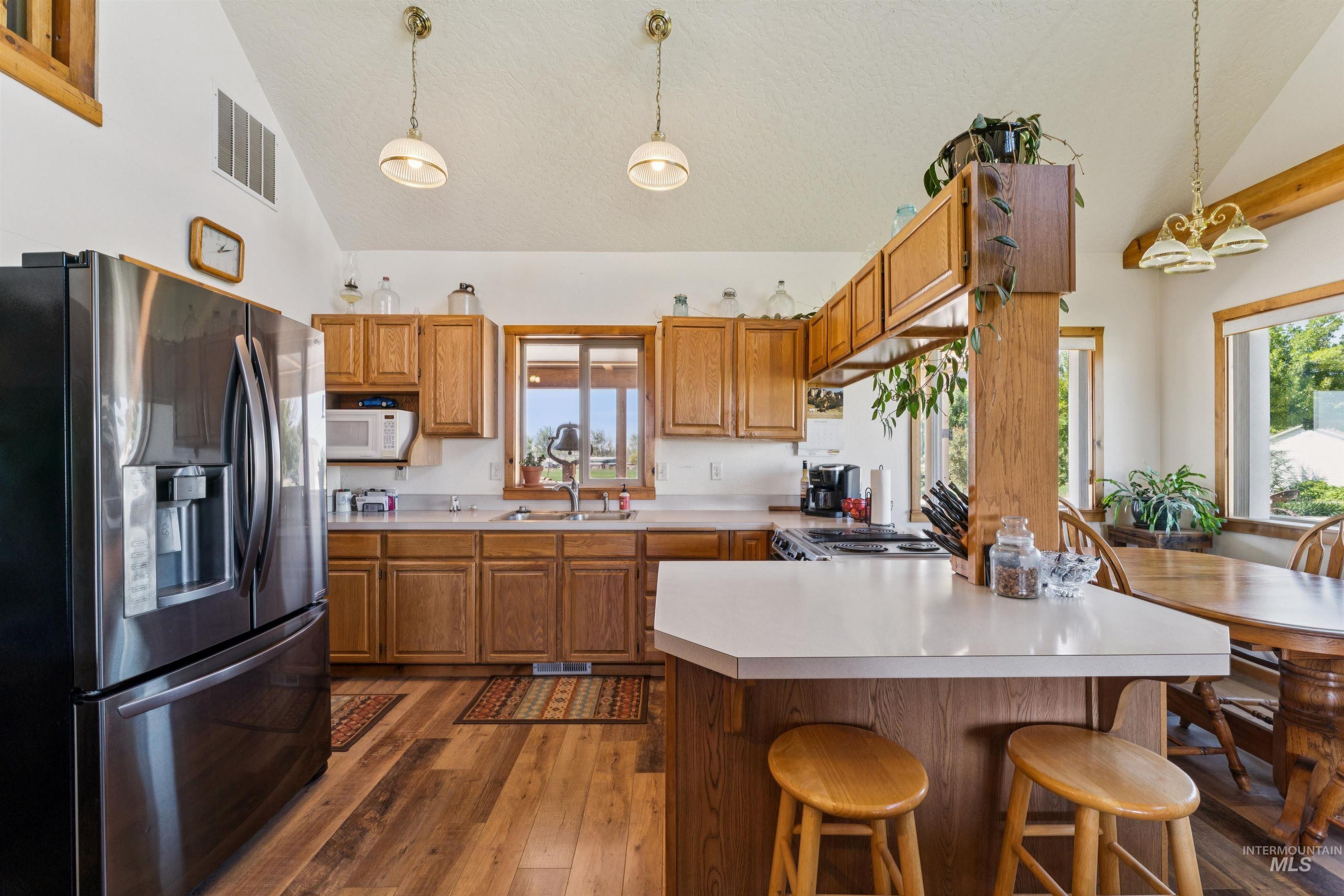 Kitchen with warm wood cabinetry, a large island, stainless steel refrigerator, and adjoining window-side dining area.