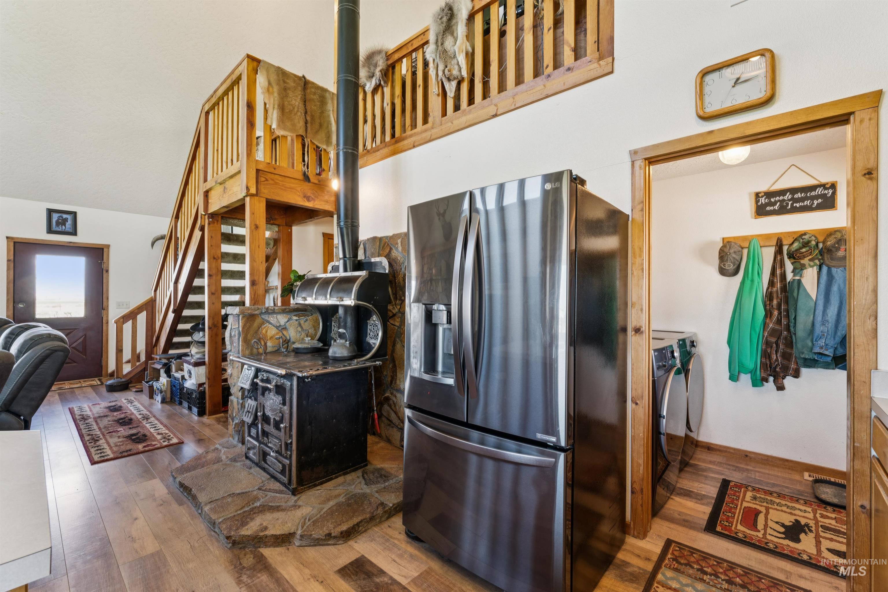 Rustic kitchen with a wood-burning cookstove, stone hearth, stainless refrigerator, and staircase to a loft.