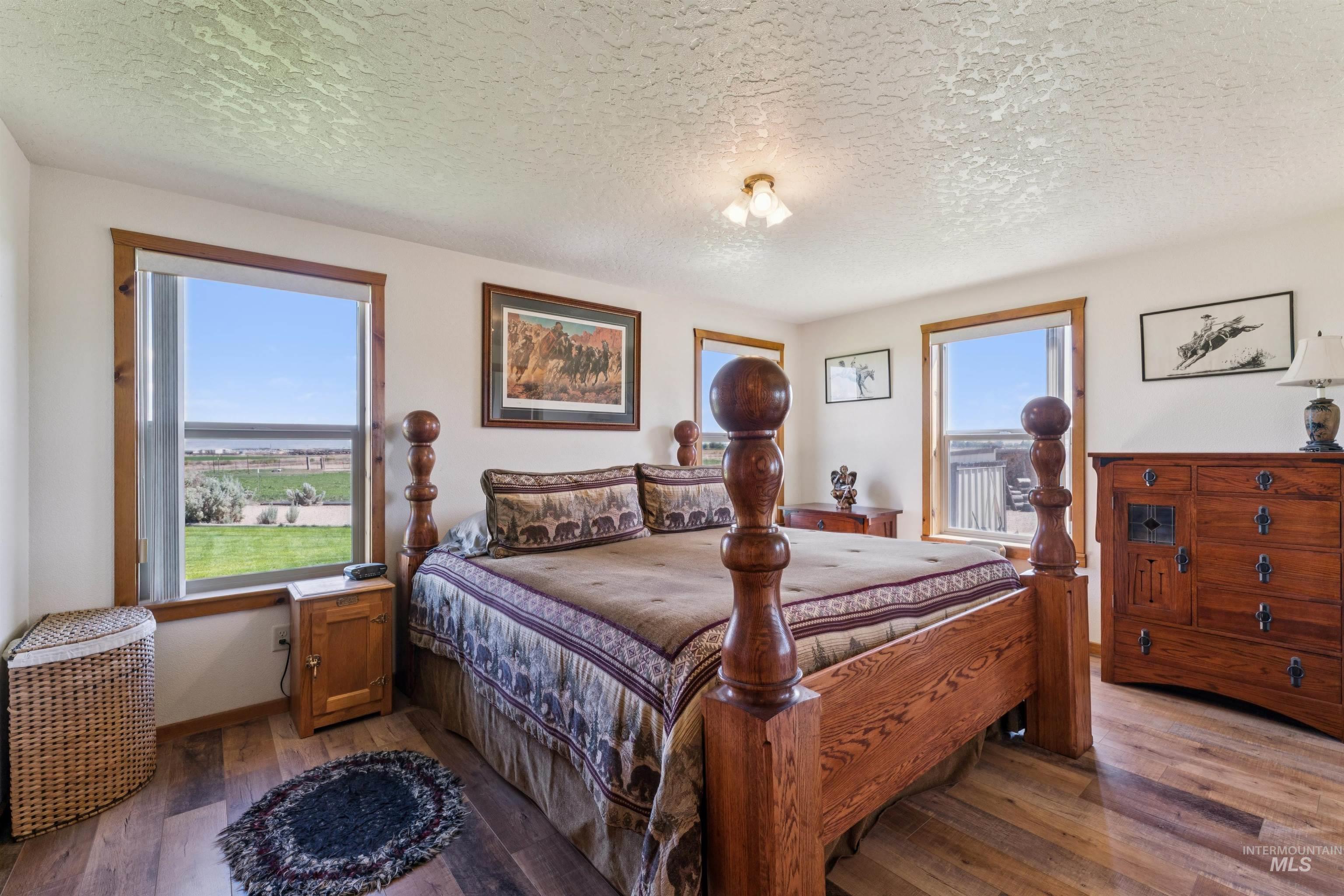 Bedroom with a wooden four-poster bed, matching dresser, and windows overlooking a green yard.
