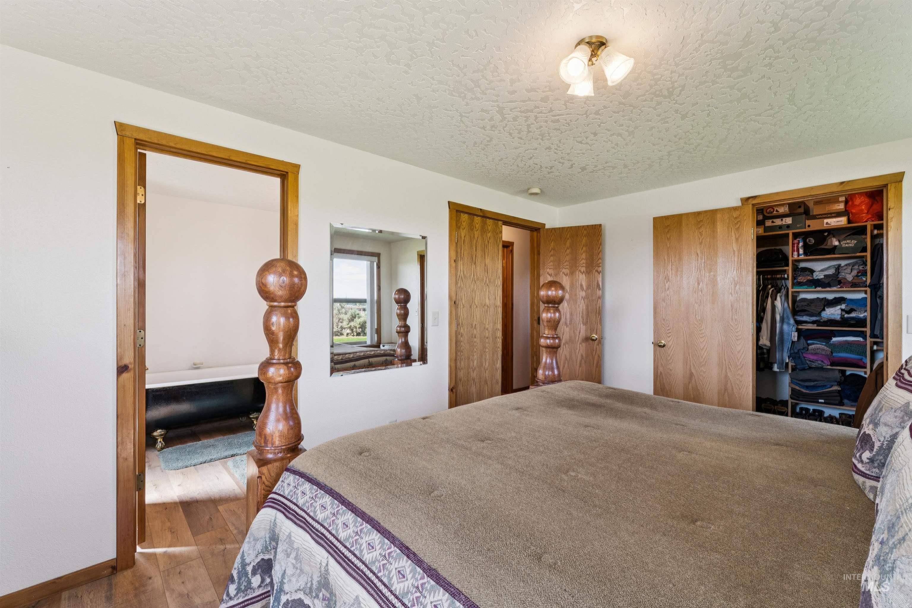 Bedroom with a large bed, open clothes closet, and adjoining bathroom with a black clawfoot tub.