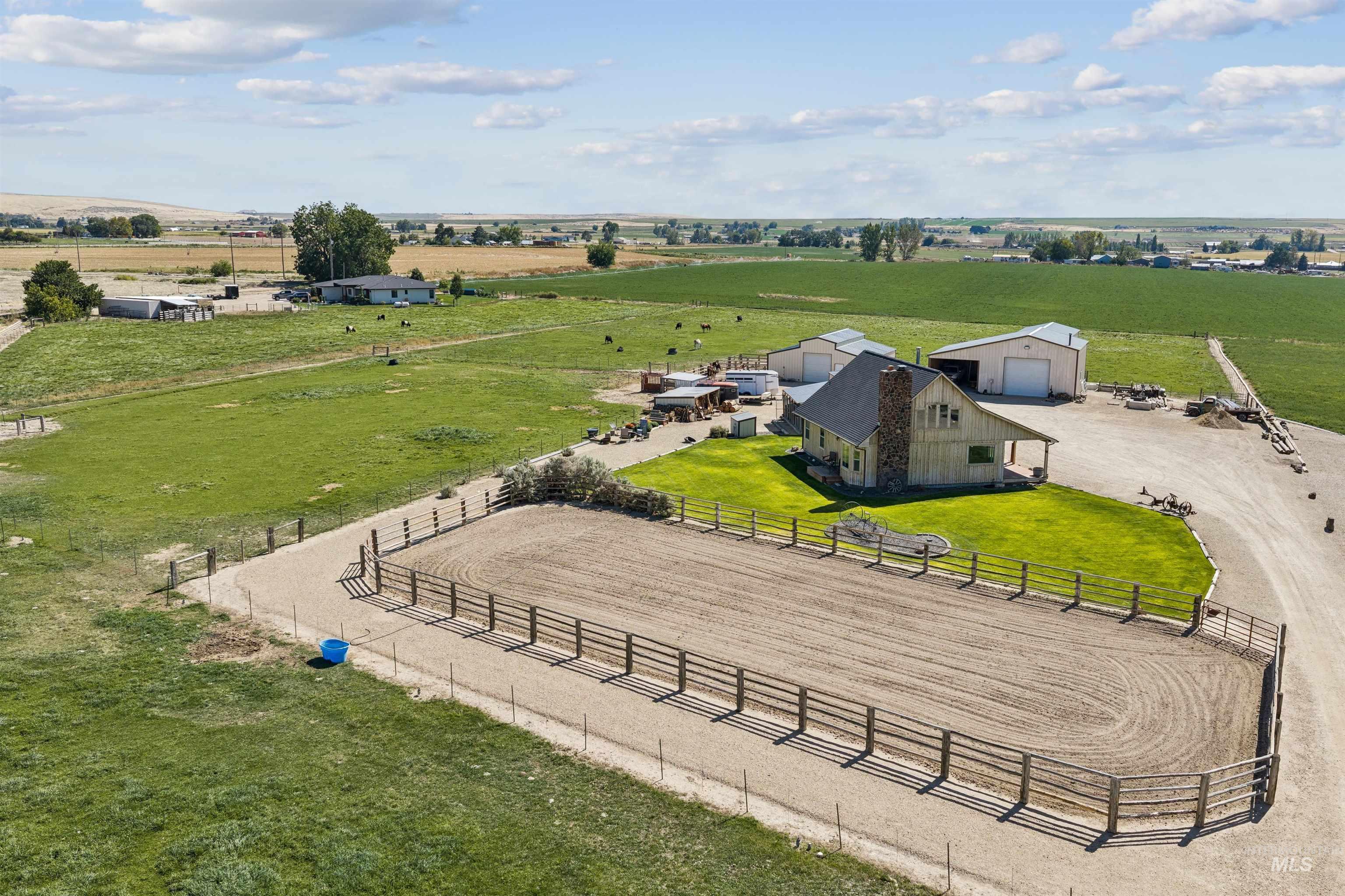 Rural property with a fenced riding arena, pasture, house, and large agricultural outbuildings.
