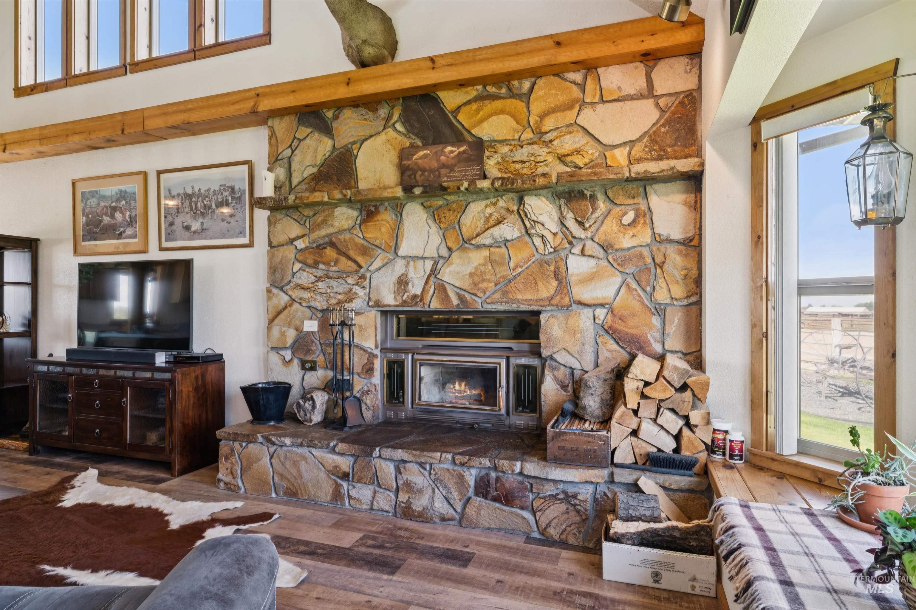 Living room with a floor-to-ceiling stone fireplace, exposed wood beam, and stacked firewood.