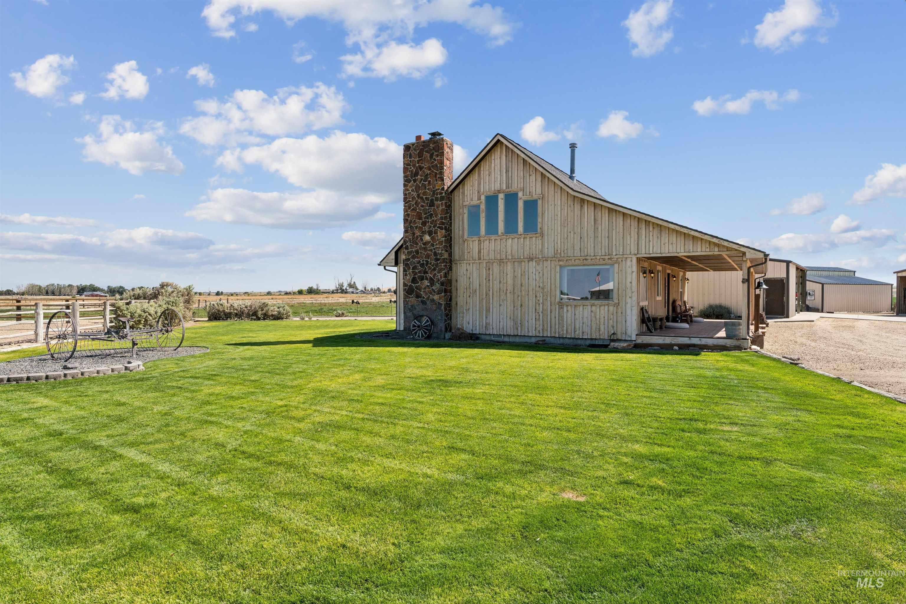 Wood-sided rural home with a stone chimney, covered porch, and expansive green lawn.