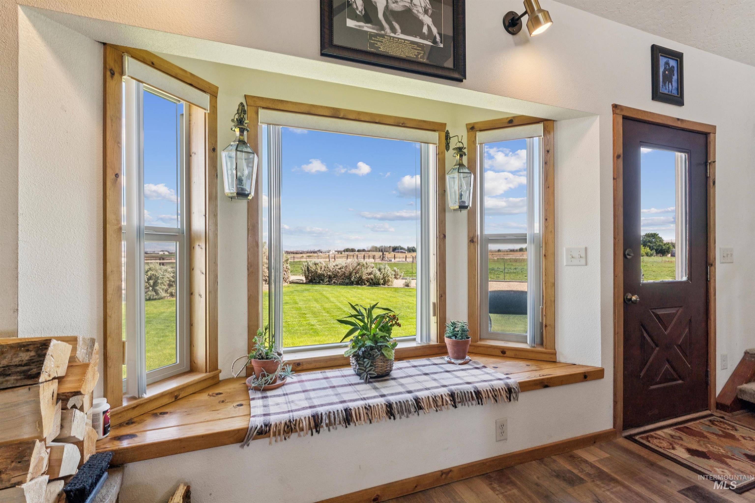 Wooden window seat with potted plants overlooking a green lawn and open fields.