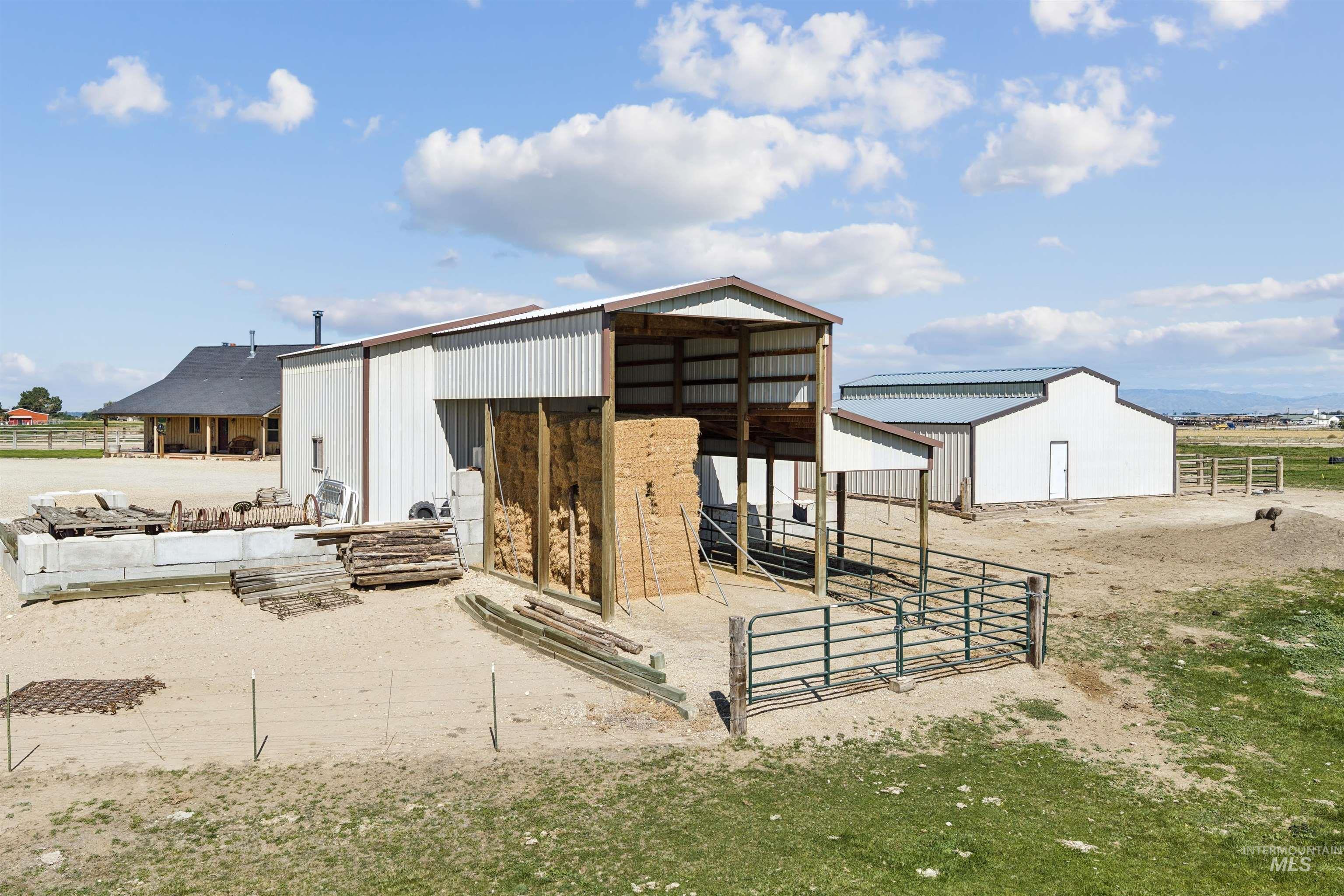 Rural property with white metal barns, a hay-filled open shed, and a gated livestock pen.