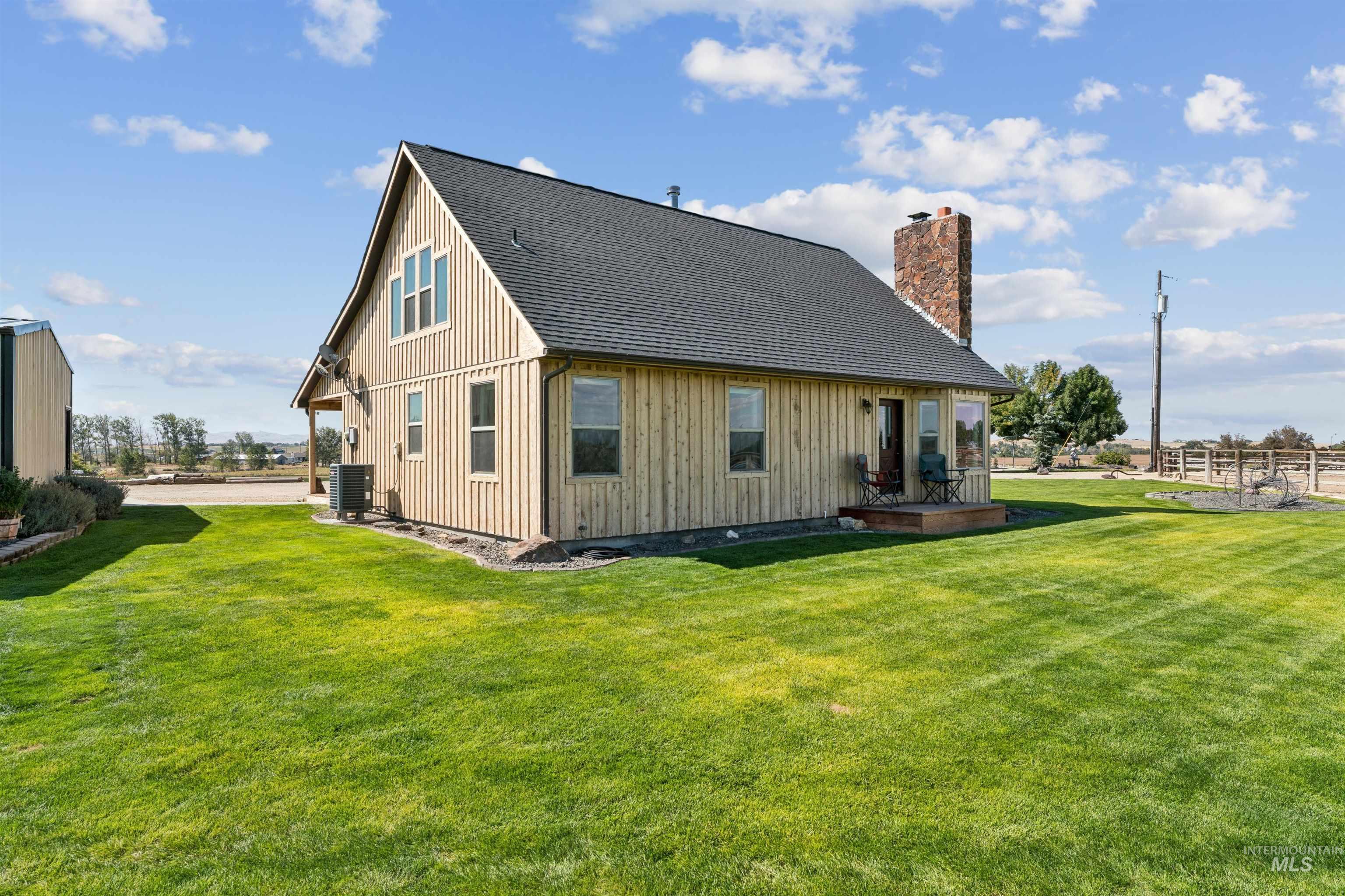 Wood-sided house with a stone chimney and small patio on a broad green lawn.