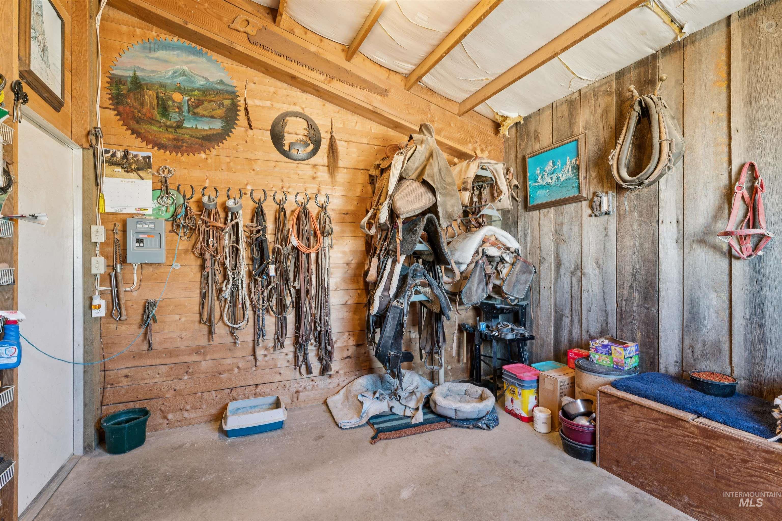 Wood-paneled tack room with saddles and bridles hanging beside animal supplies and bedding.