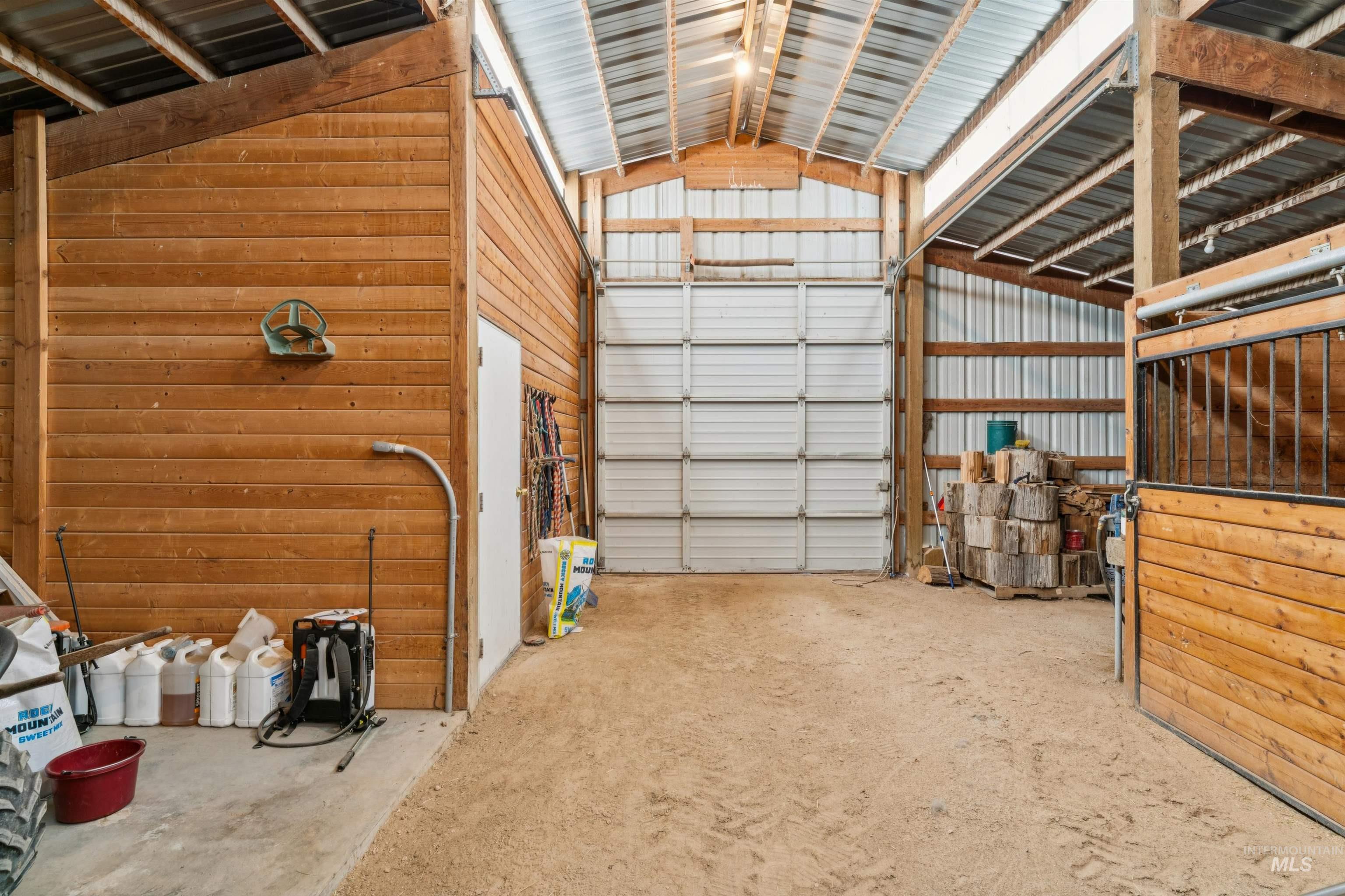 Barn interior with a large sliding door, wooden horse stall, and stacked firewood.