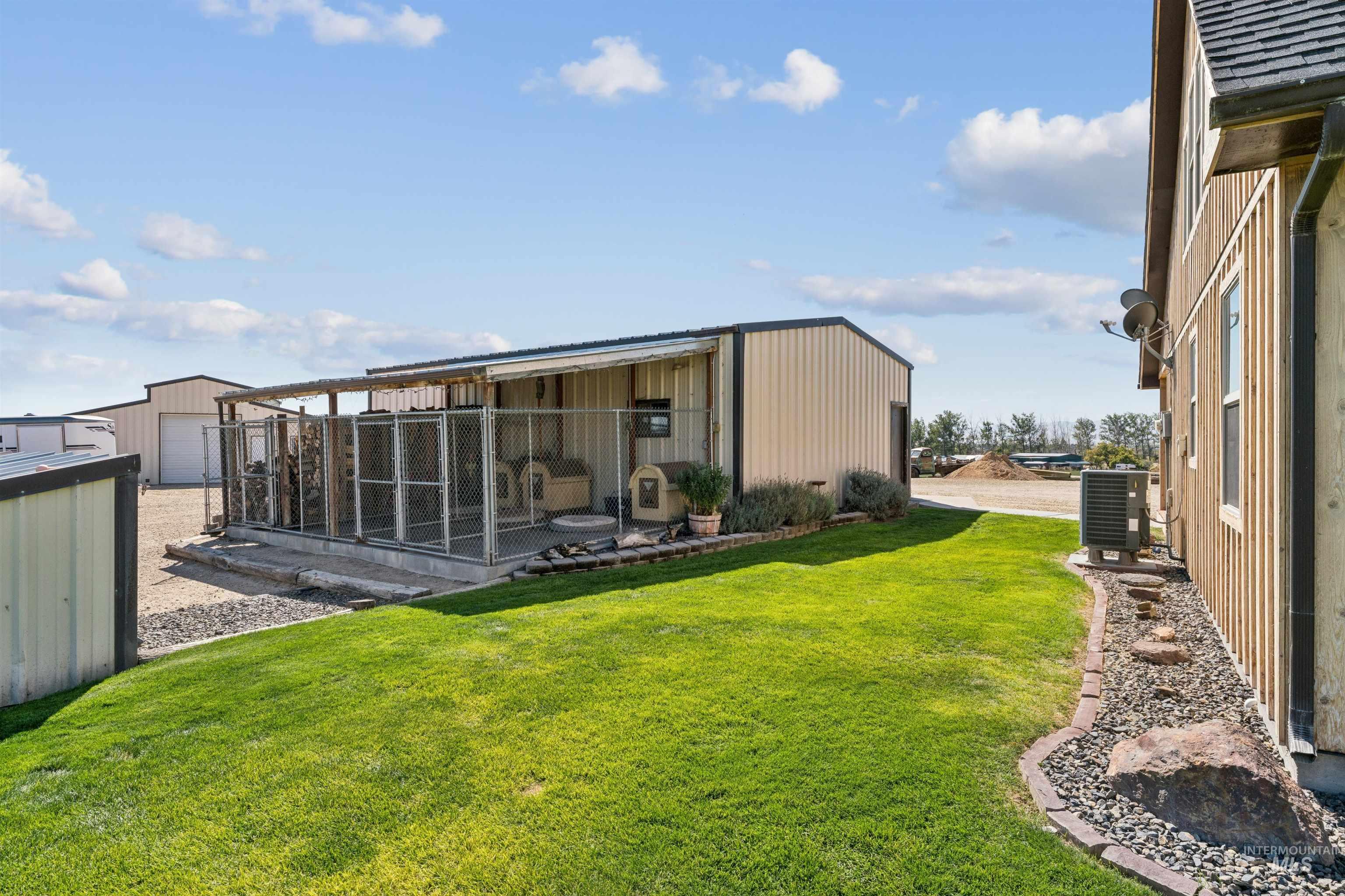 Green lawn beside a fenced covered kennel and metal outbuildings.