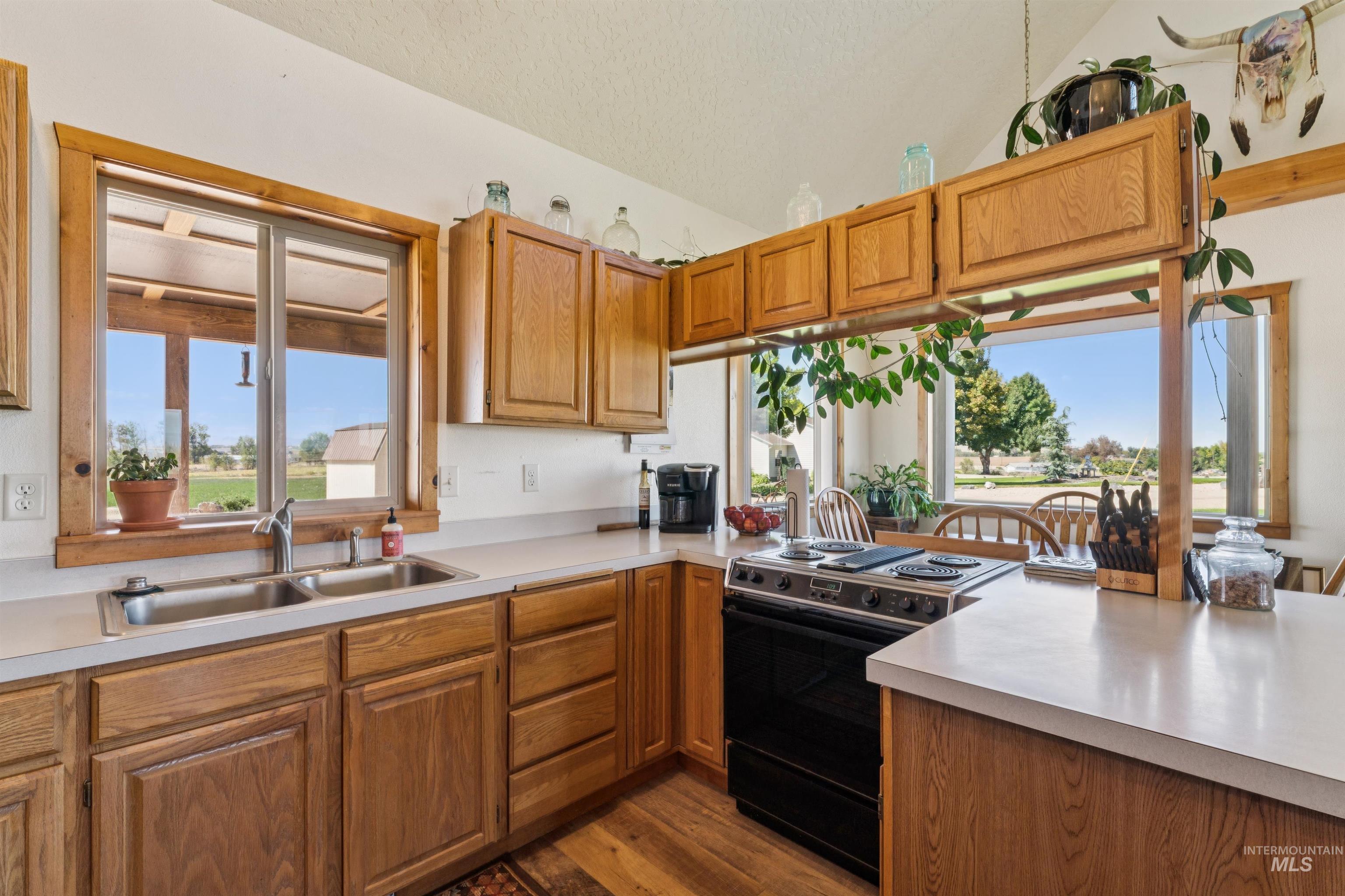 Kitchen with honey-toned wood cabinets, a double sink beneath a window, and a black range beside a peninsula.