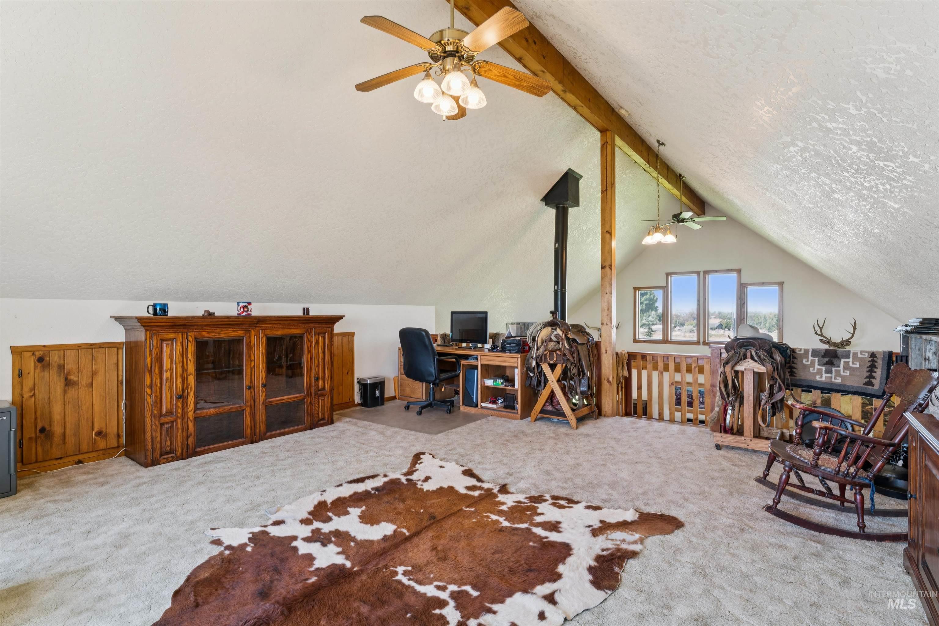 Furnished loft with exposed wood beams, a wood-burning stove, and a cowhide rug.