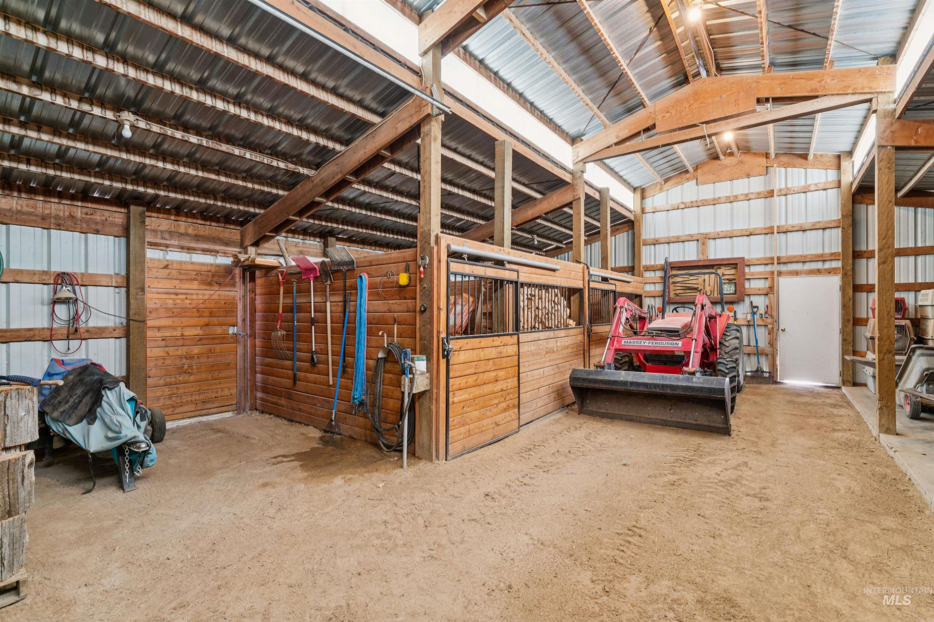 Barn interior with wooden horse stalls and a red tractor beneath exposed timber rafters.