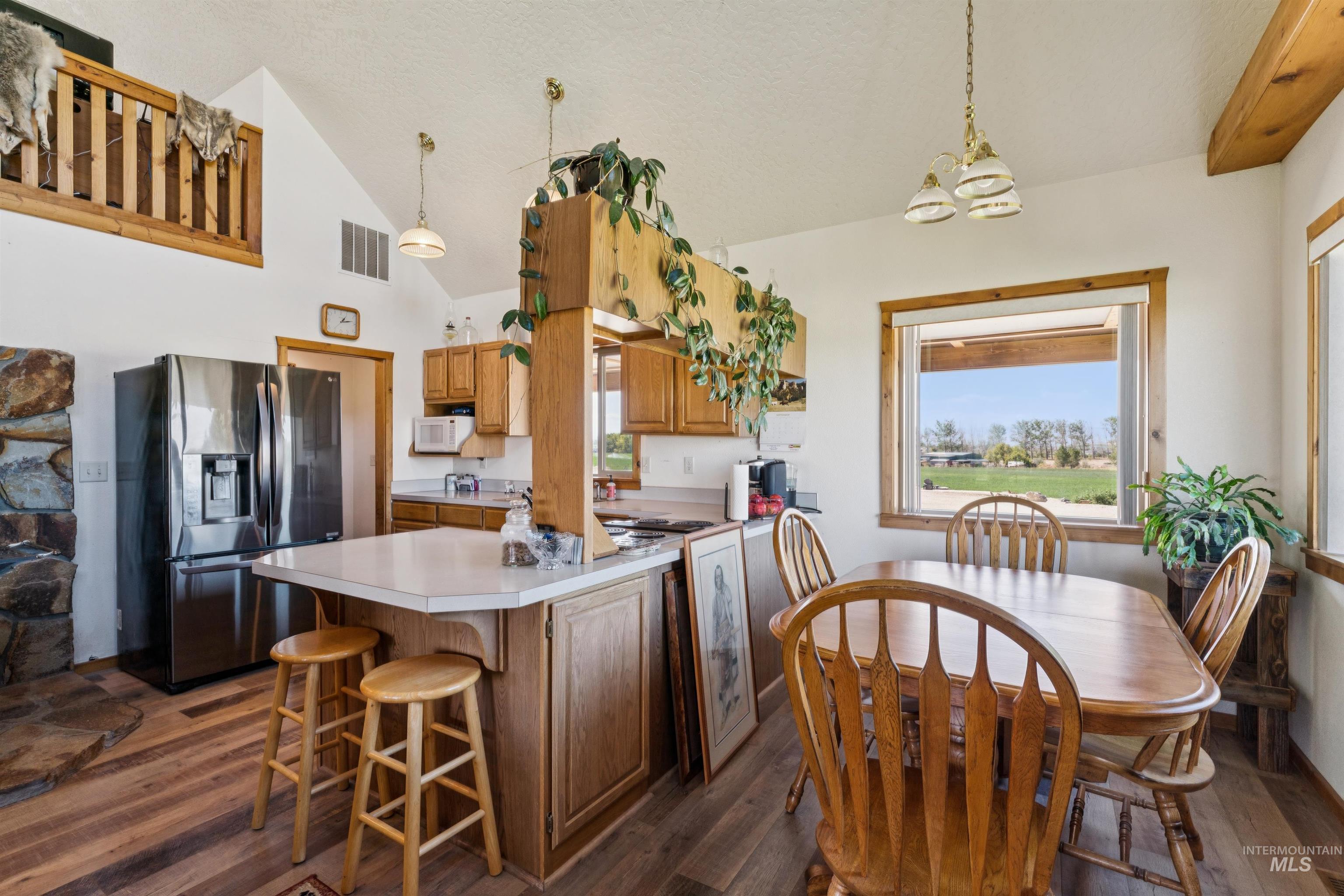 Kitchen and dining area with wood cabinetry, stainless steel appliances, and a large window overlooking a green yard.