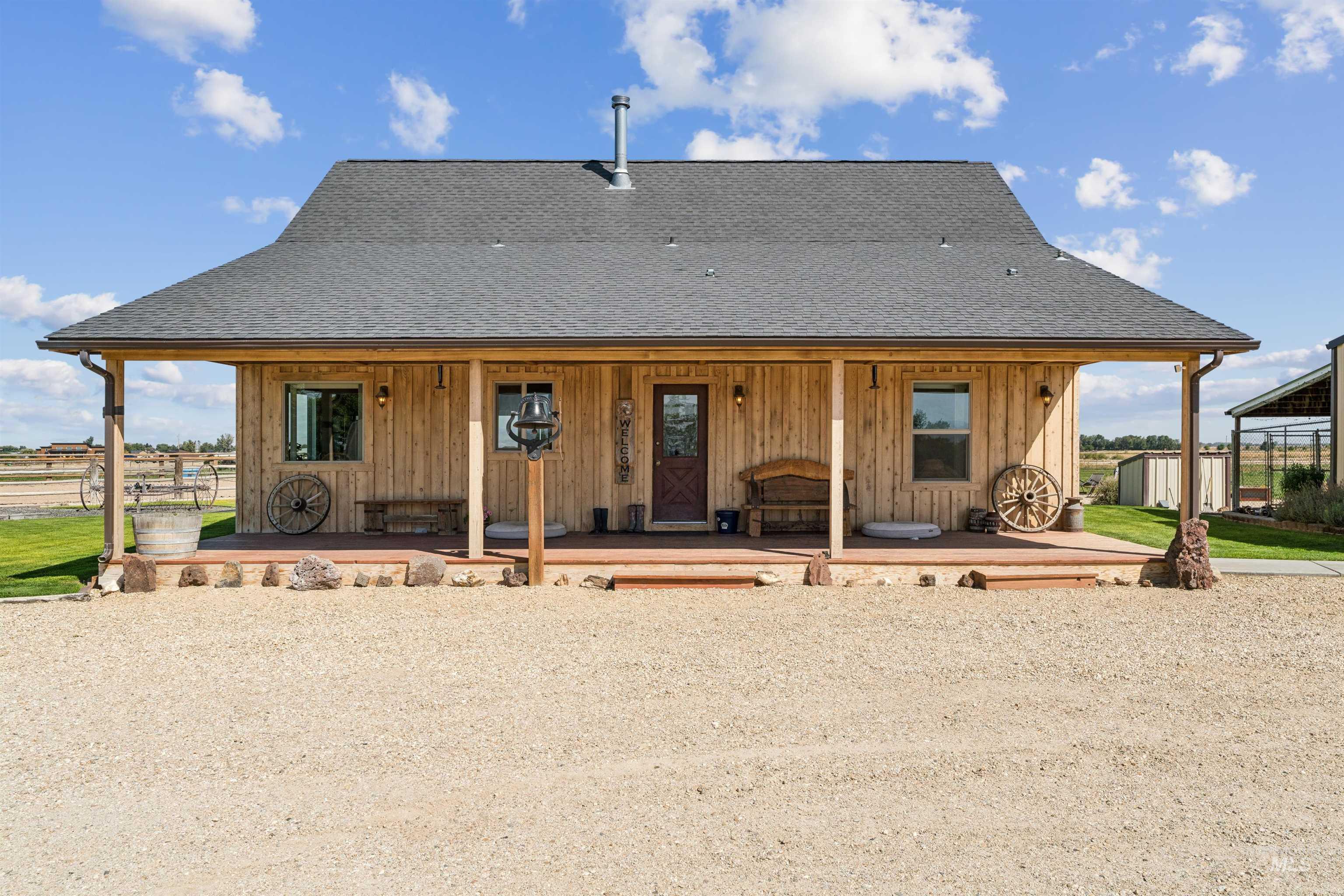 Rustic wood-sided home with a wide covered porch, wagon wheels, and gravel forecourt.