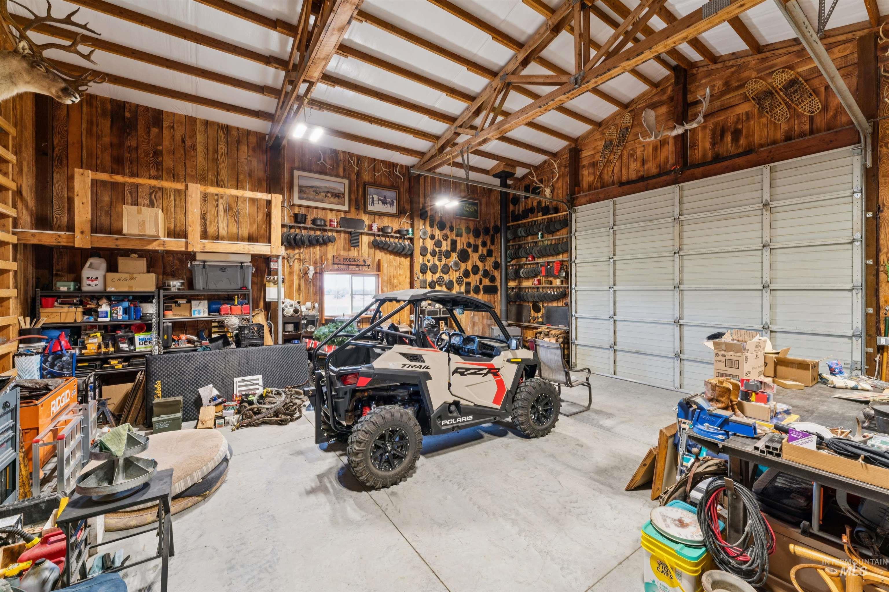 Workshop garage with exposed timber trusses, a Polaris RZR, storage shelves, and a large sectional door.