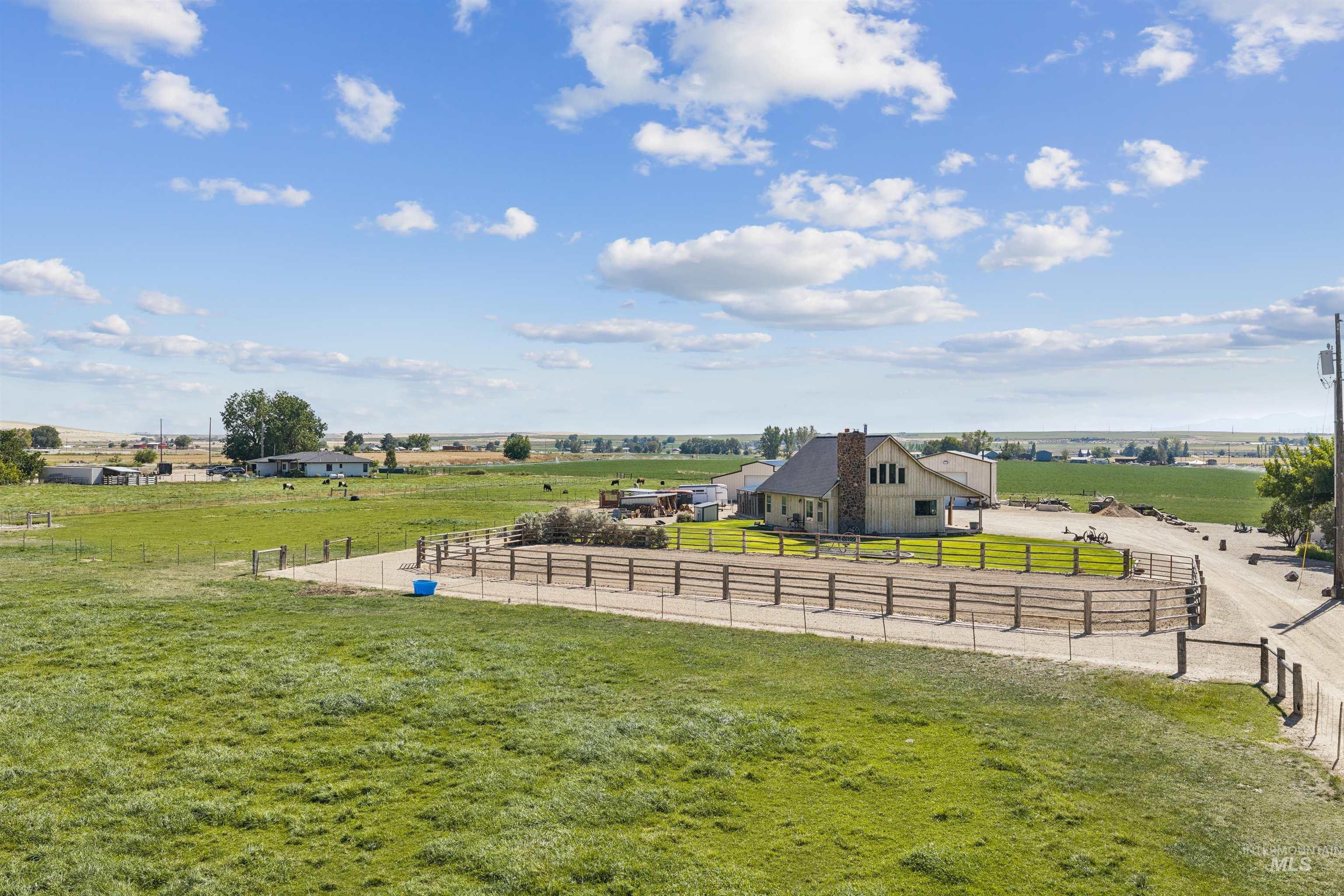 Rural farmhouse with a stone chimney, fenced paddock, and broad green pasture.