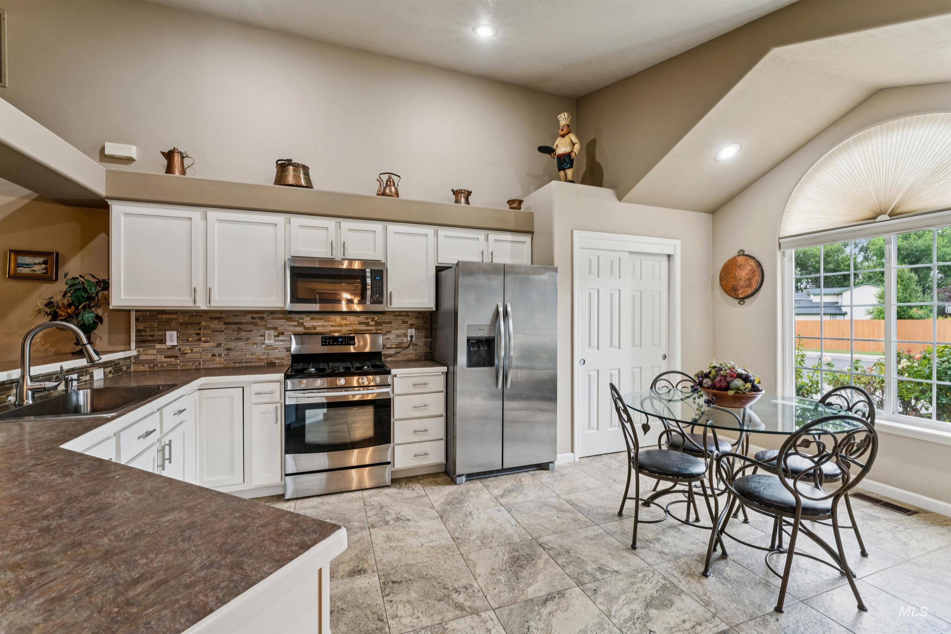 Kitchen with white cabinets and stainless steel appliances beside a glass dining table and arched window.