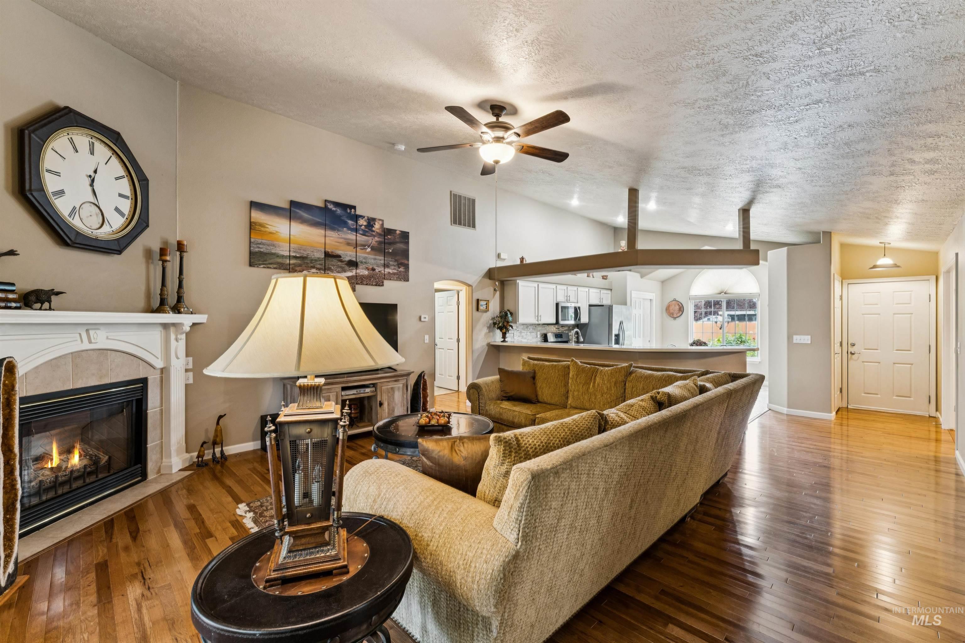 Living room with a fireplace, large sectional, hardwood floors, and an open kitchen.