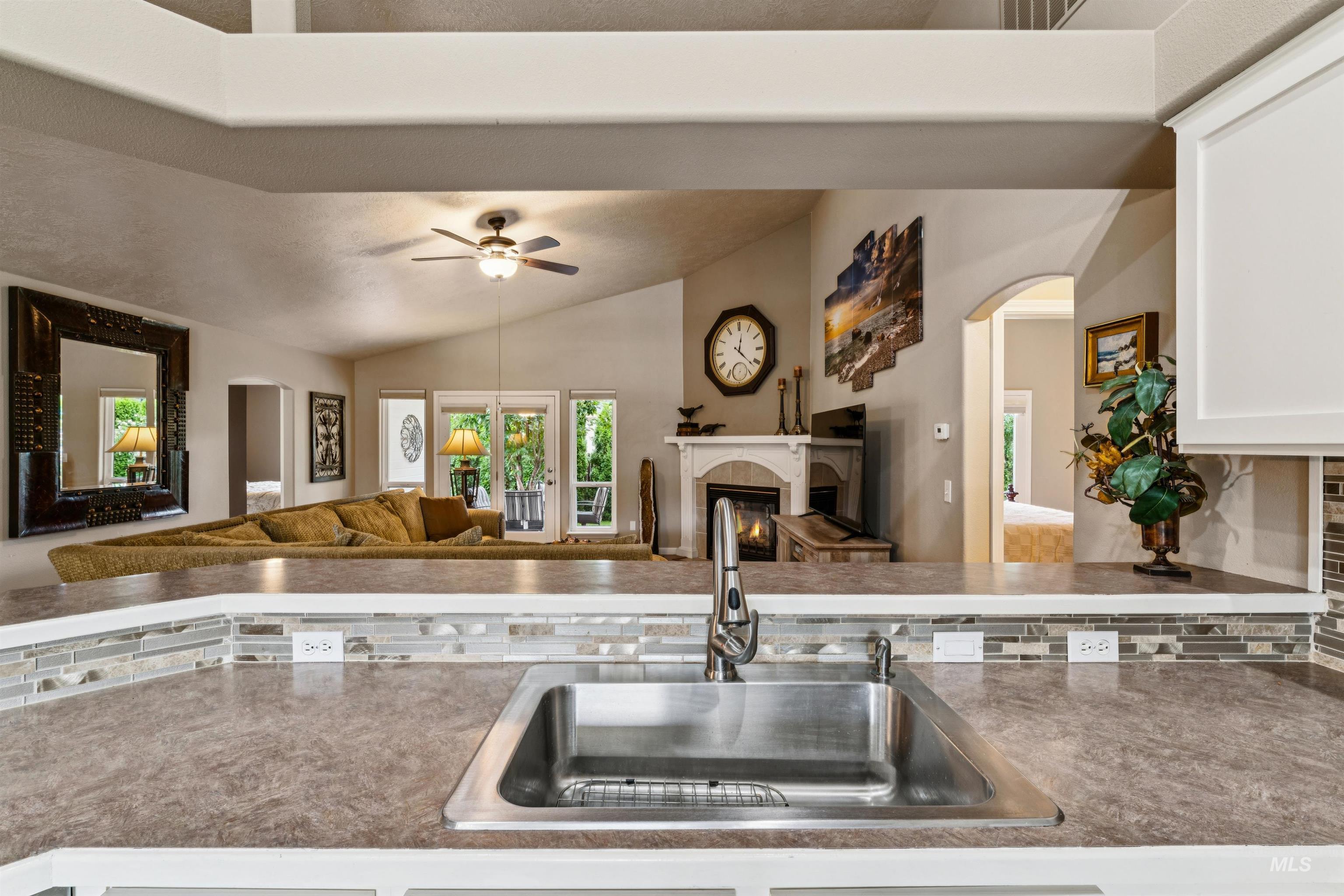 Kitchen sink and stone counter overlook a furnished living room with a fireplace and glass doors.