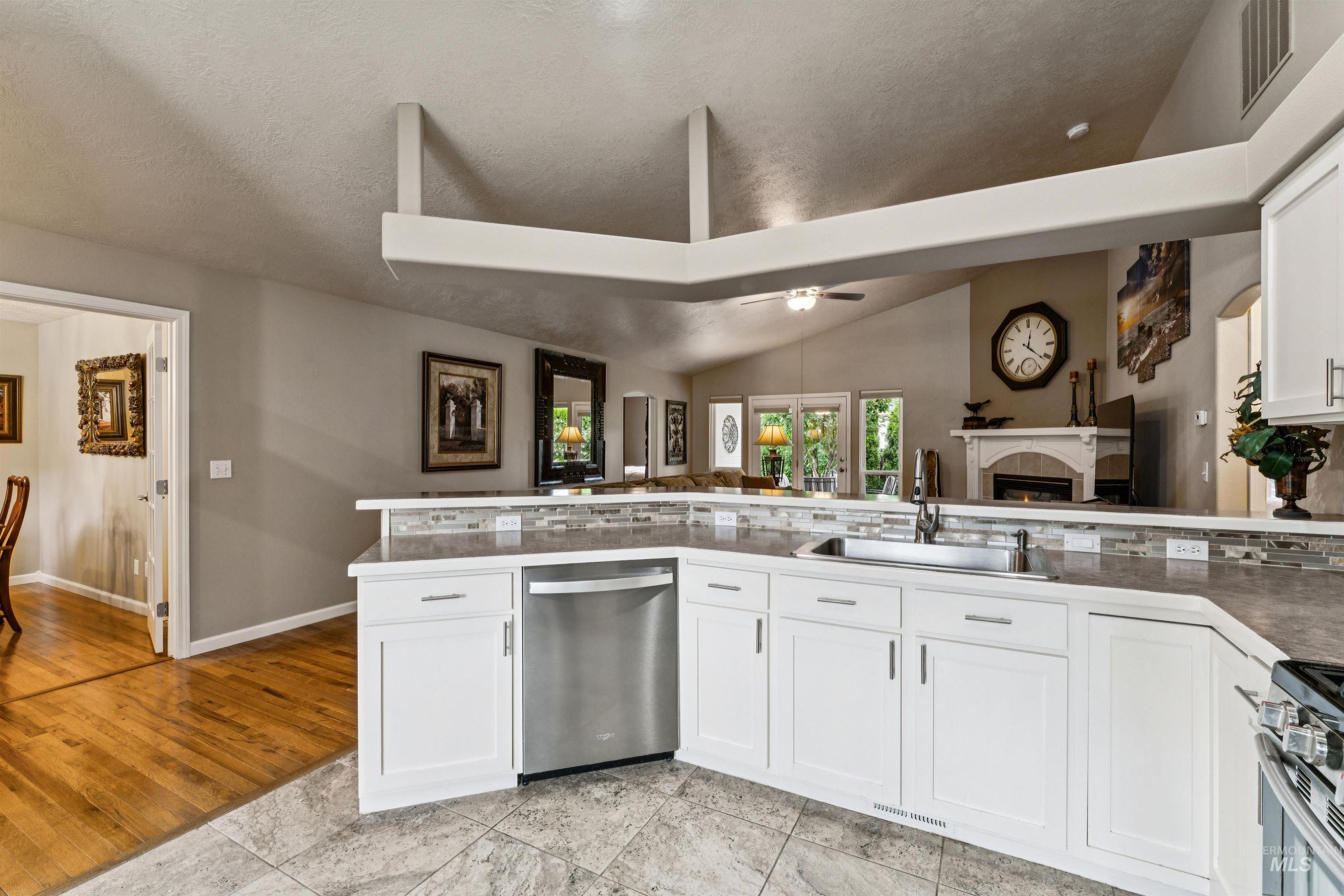Kitchen with white cabinets and a raised breakfast bar opening to a living room with a fireplace.