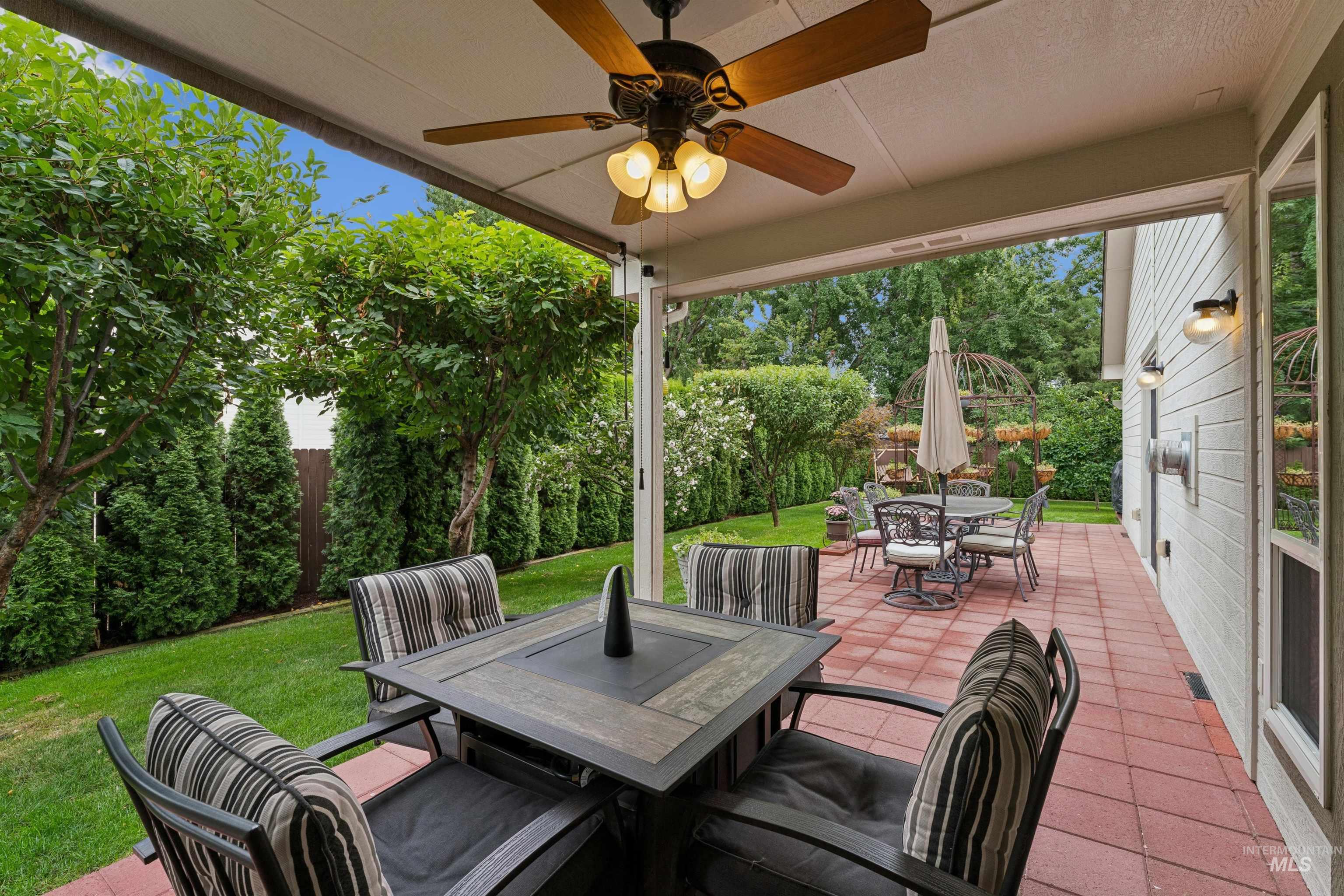 Covered patio with cushioned seating, red pavers, and a leafy, fenced backyard.