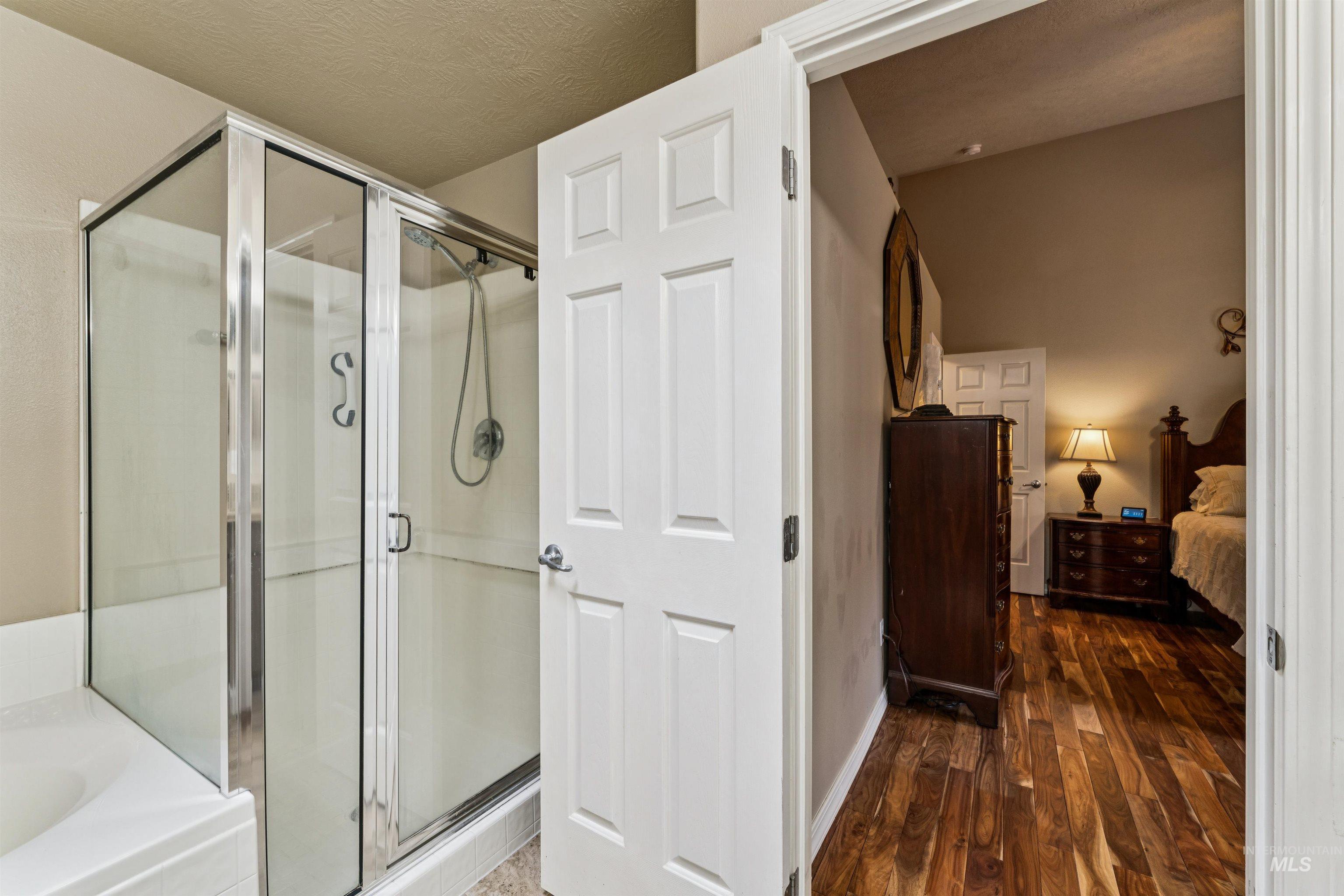 Bathroom with glass-enclosed shower and tub, opening onto a furnished bedroom.