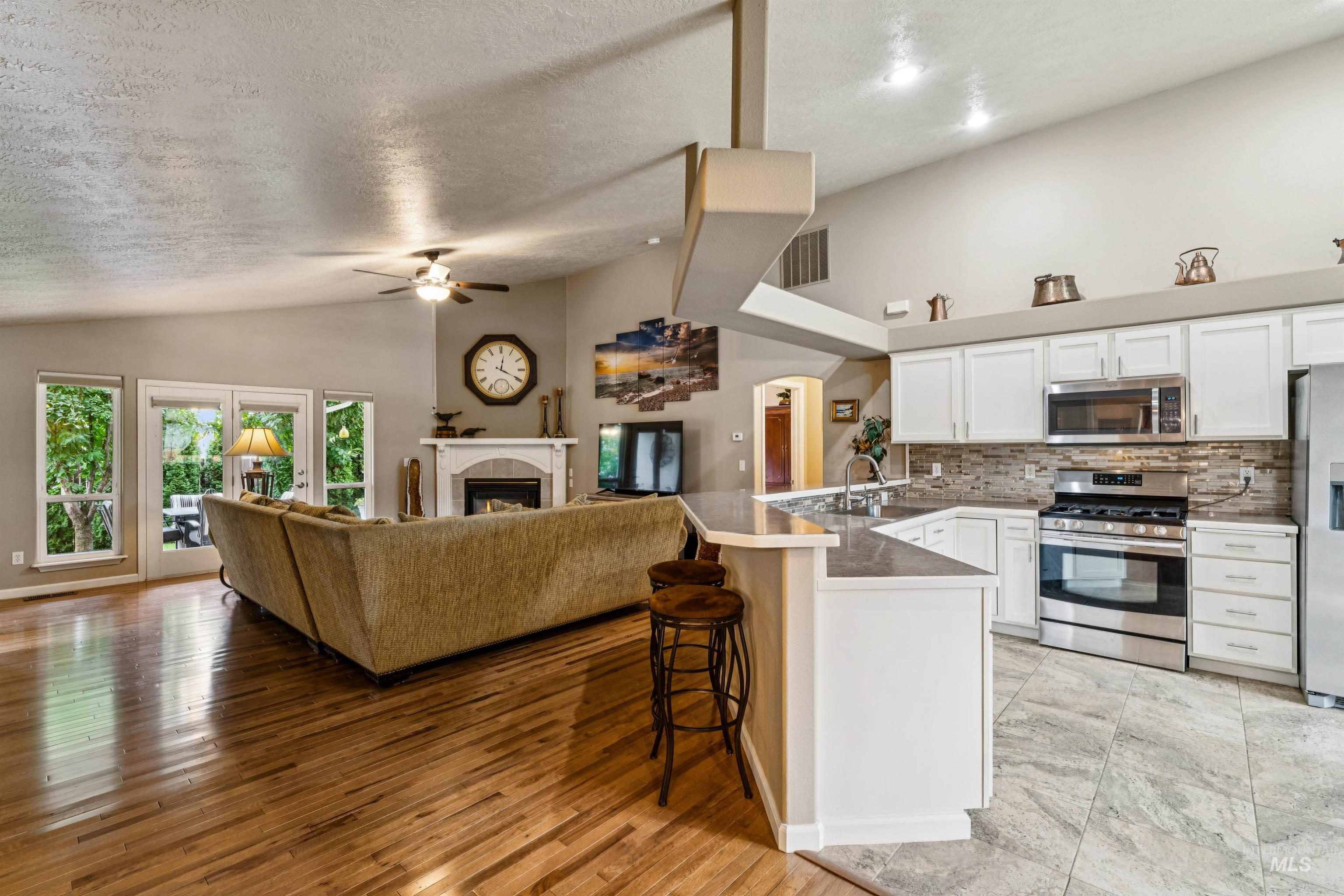 Open-plan living room and kitchen with vaulted ceilings, a fireplace, and white cabinetry.