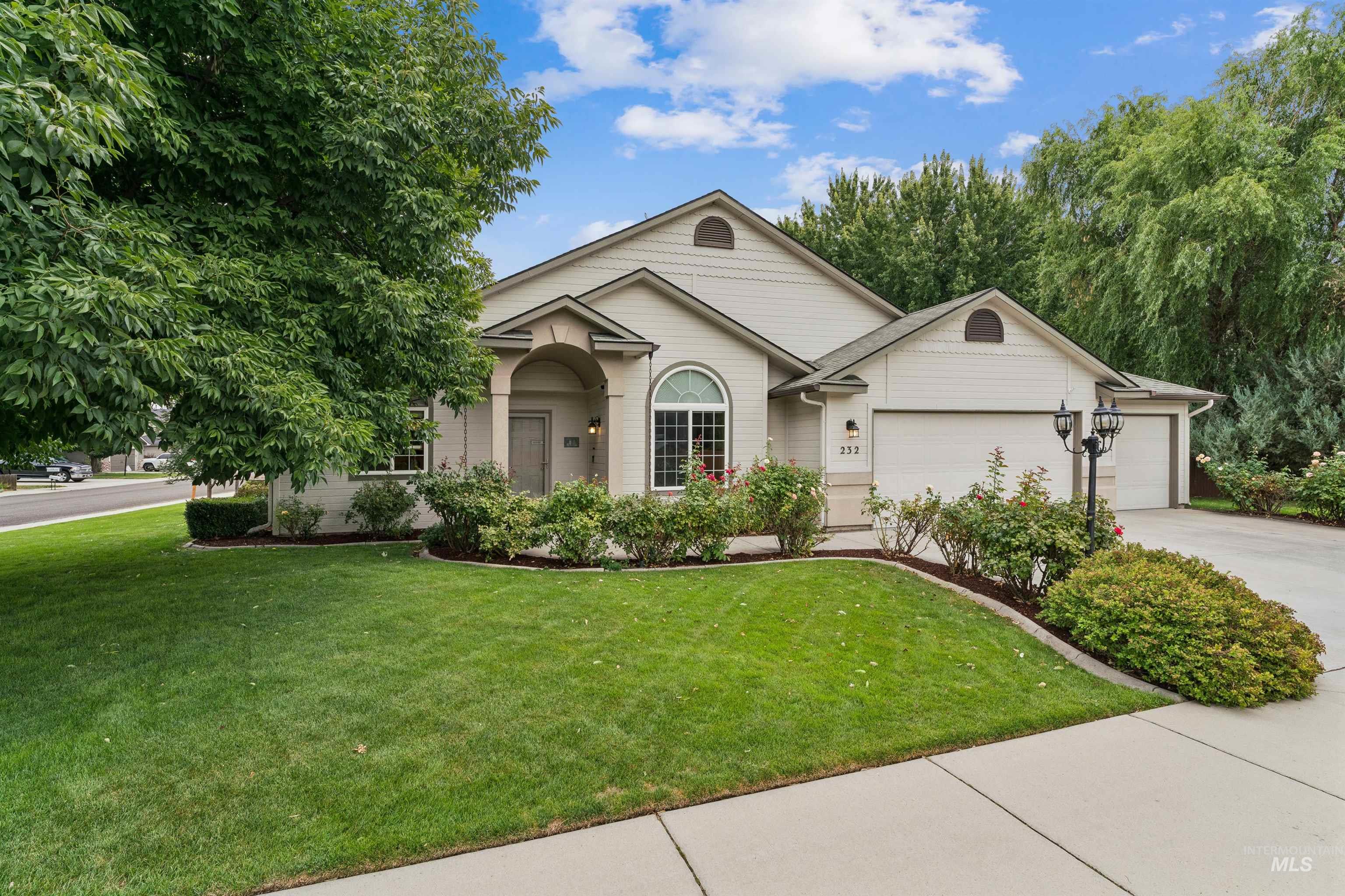 Light-colored home with an arched entry, attached garage, rose bushes, and a landscaped lawn.