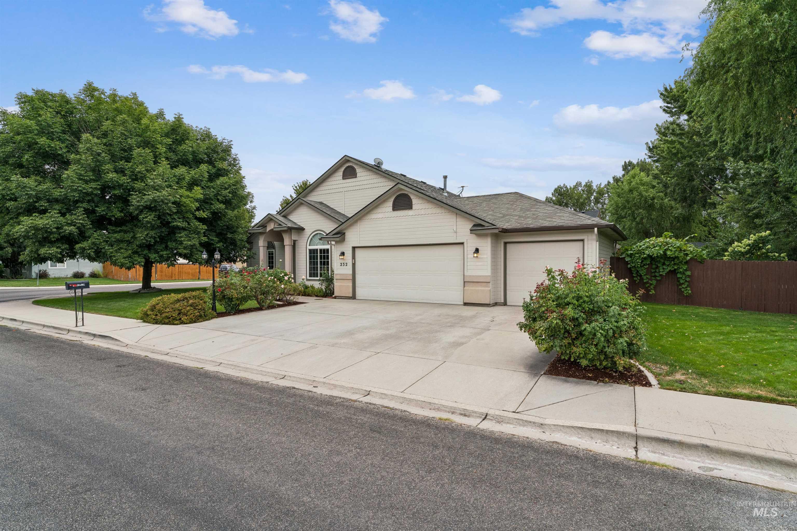 Beige home with a two-car garage, wide driveway, and landscaped front yard.