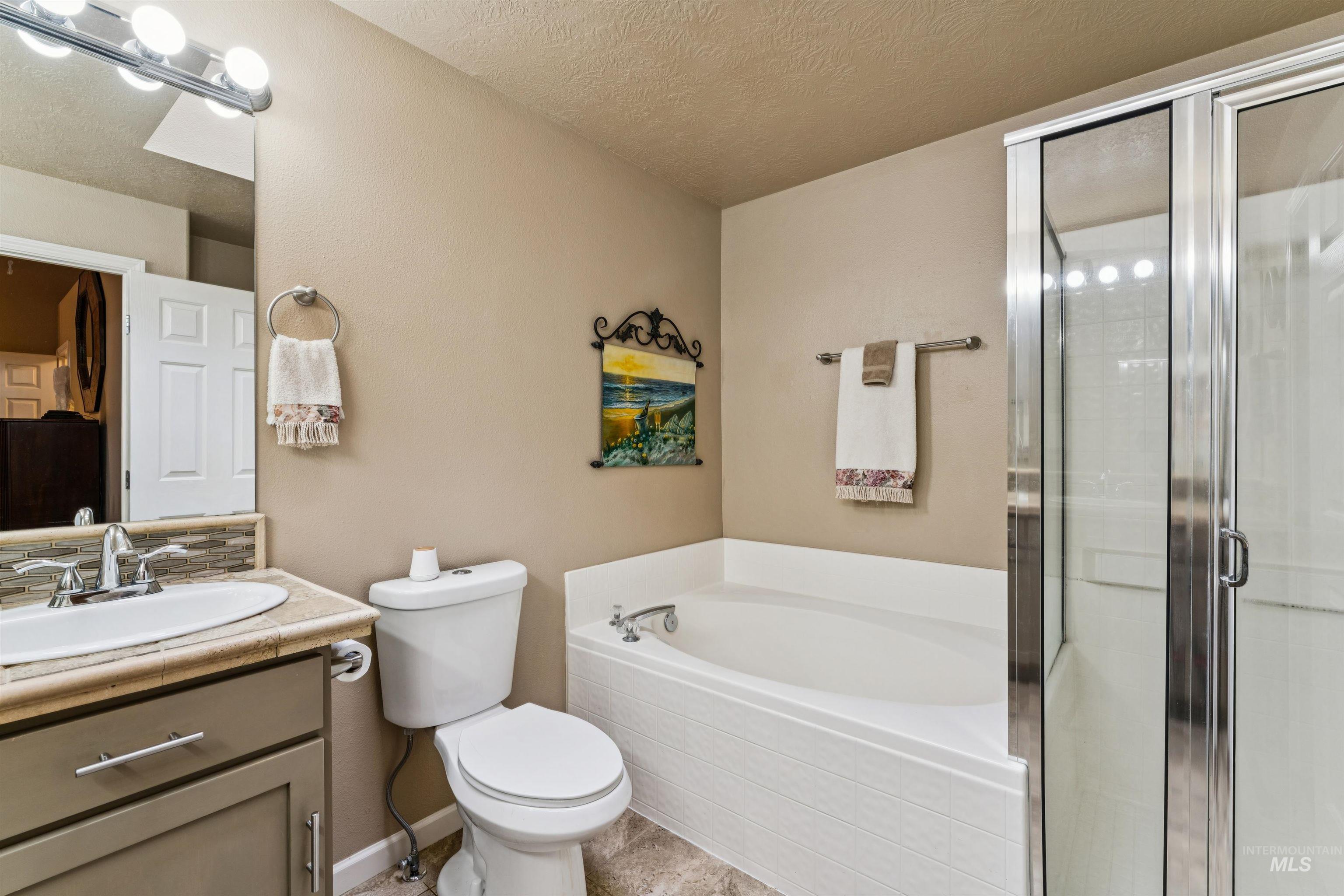 Bathroom with a white bathtub, glass-enclosed shower, toilet, and vanity sink.