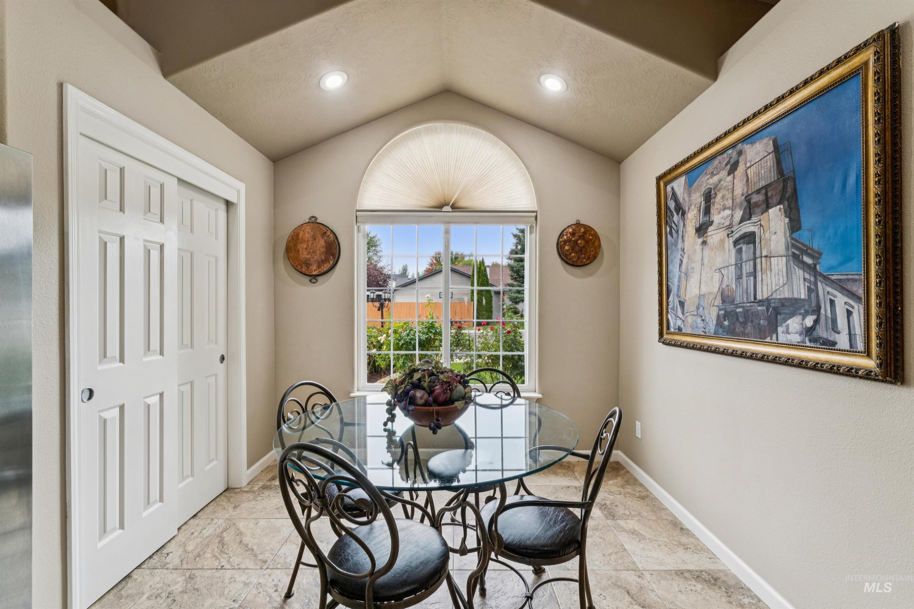 Dining nook with glass table, wrought-iron chairs, and an arched garden-view window.