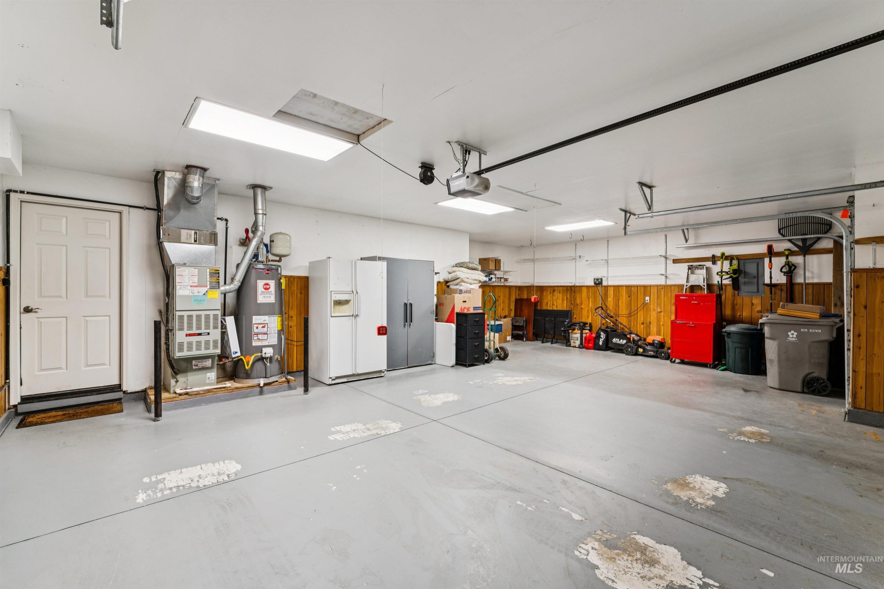 Spacious garage with refrigerators, furnace, lawn equipment, and red tool cabinets along the walls.