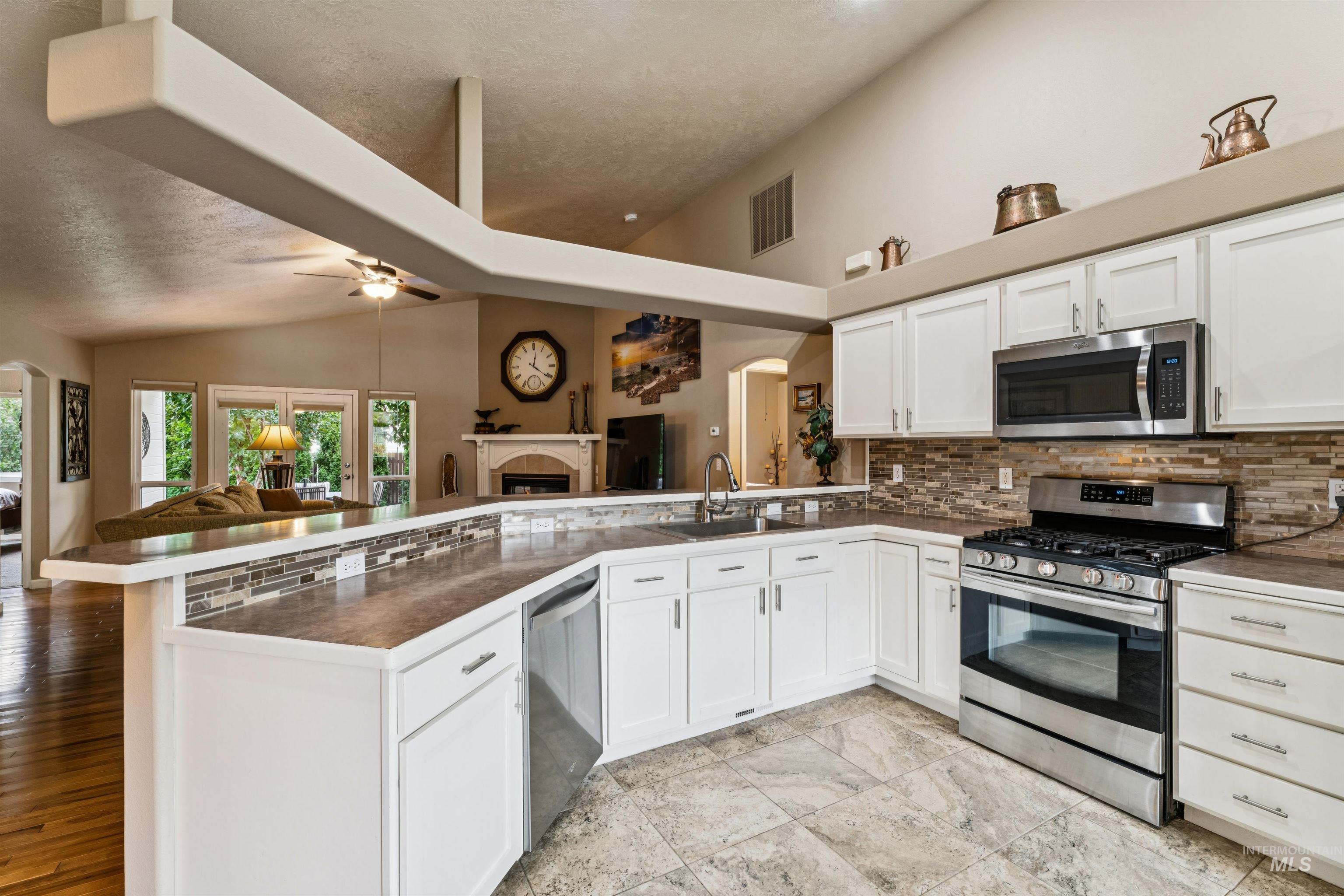 Open kitchen with white cabinets, stainless steel appliances, and a long breakfast bar overlooking the living room.