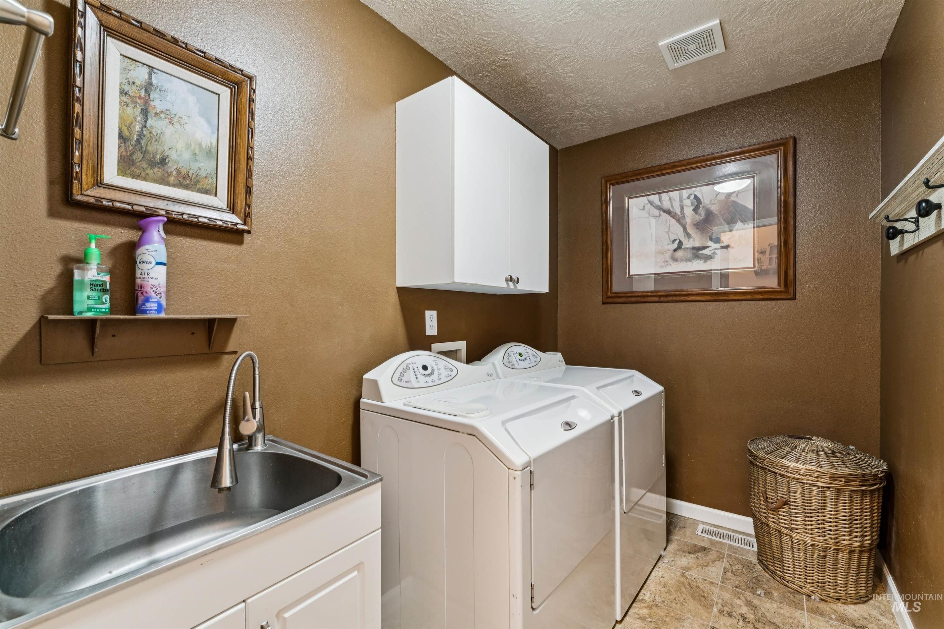Laundry room with white washer and dryer, utility sink, wall cabinets, and wicker hamper.