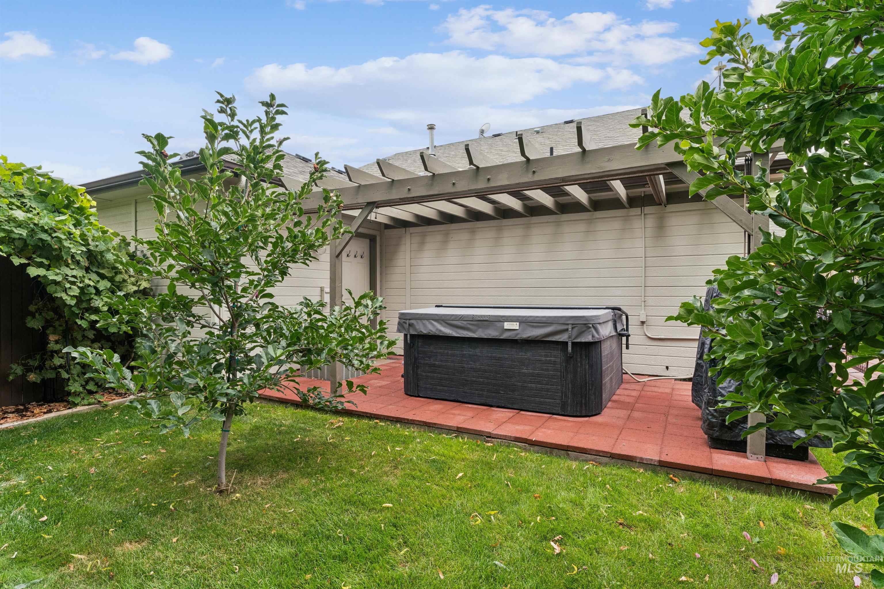 Backyard hot tub beneath a wooden pergola on a red-paver patio.