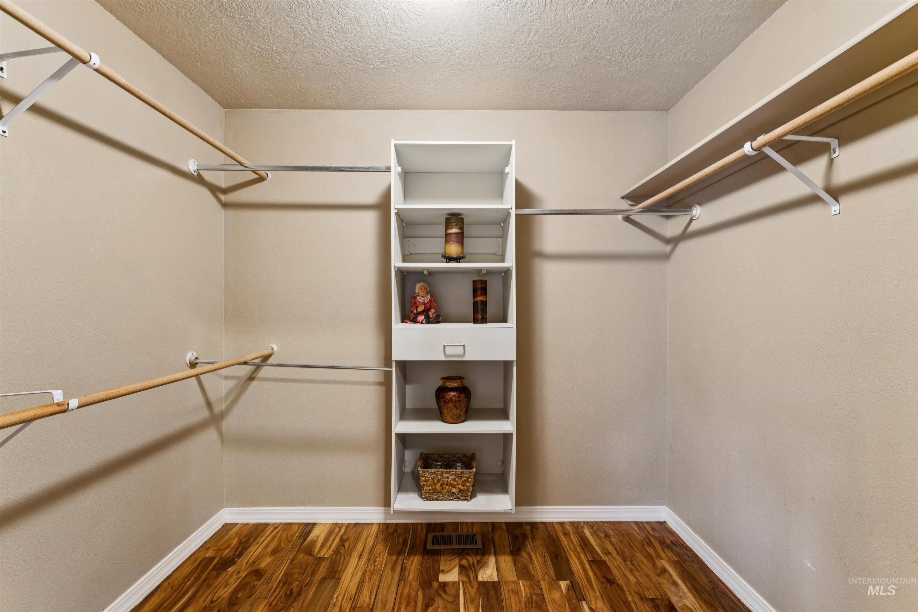 Walk-in closet with wood flooring, side-mounted hanging rods, and a central white shelving unit.