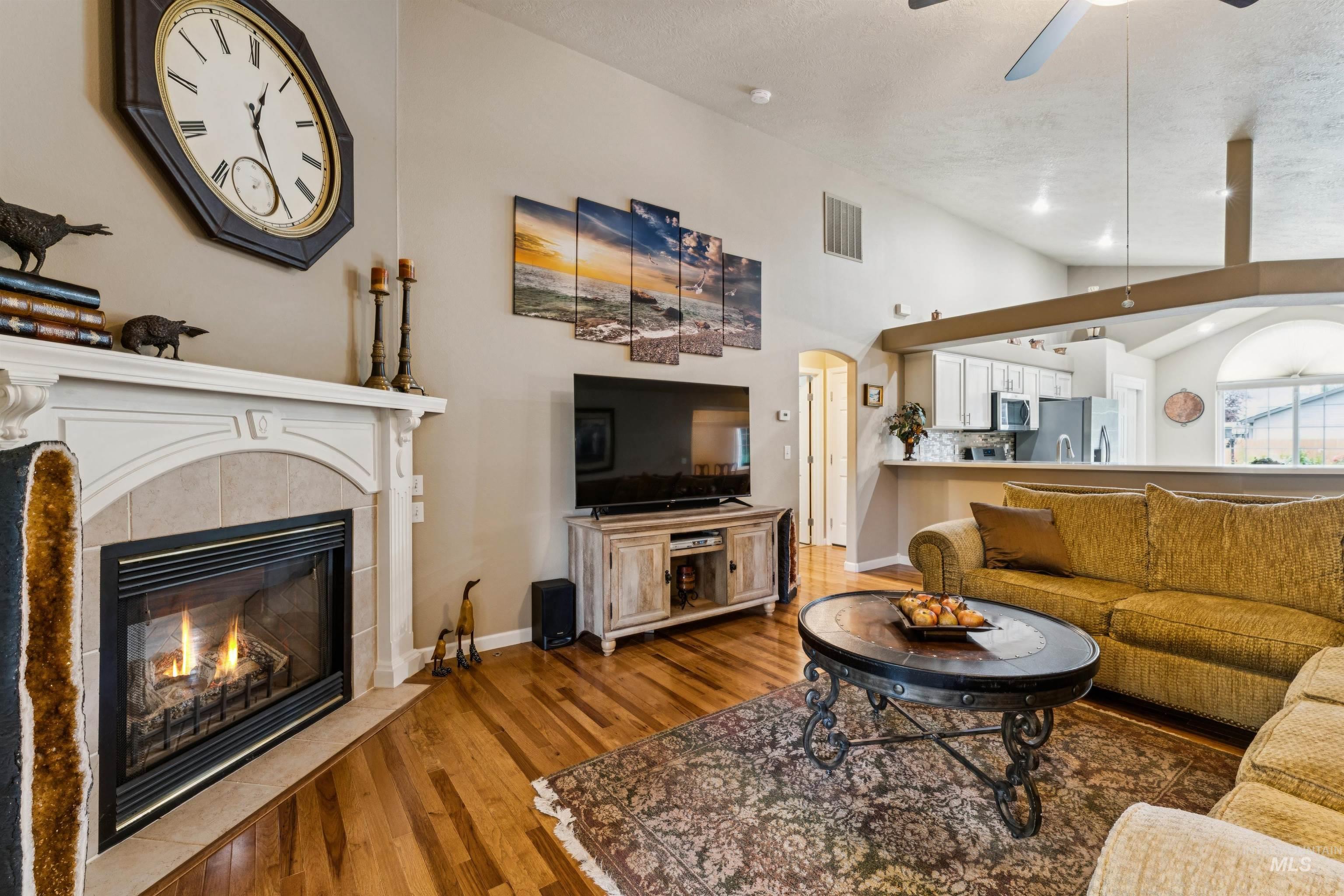 Open living room with a lit fireplace, mustard sofa, hardwood floors, and a view into the kitchen.
