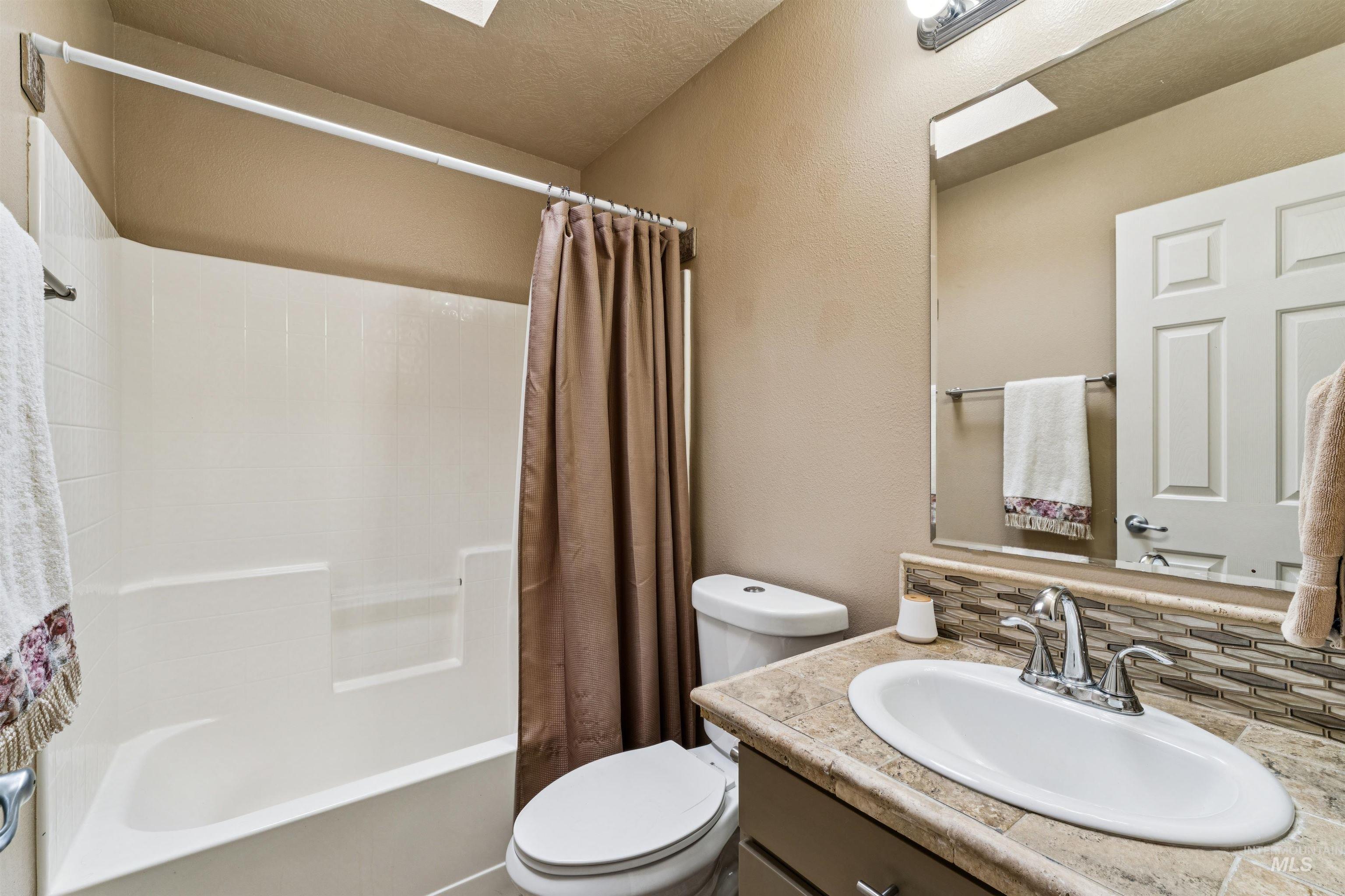 Bathroom with a white tub, brown shower curtain, and vanity with a tiled backsplash.