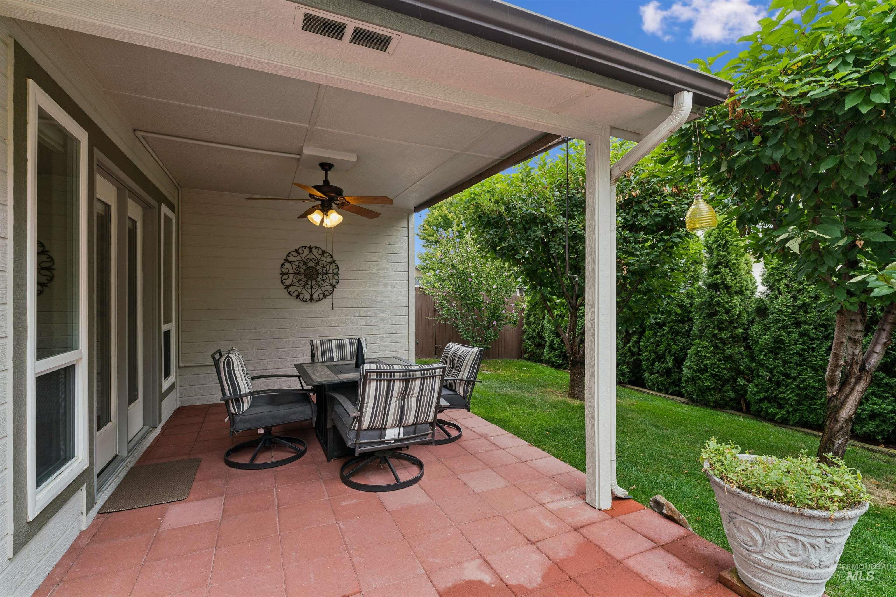 Covered patio with red tile flooring and cushioned dining set beside a leafy backyard.