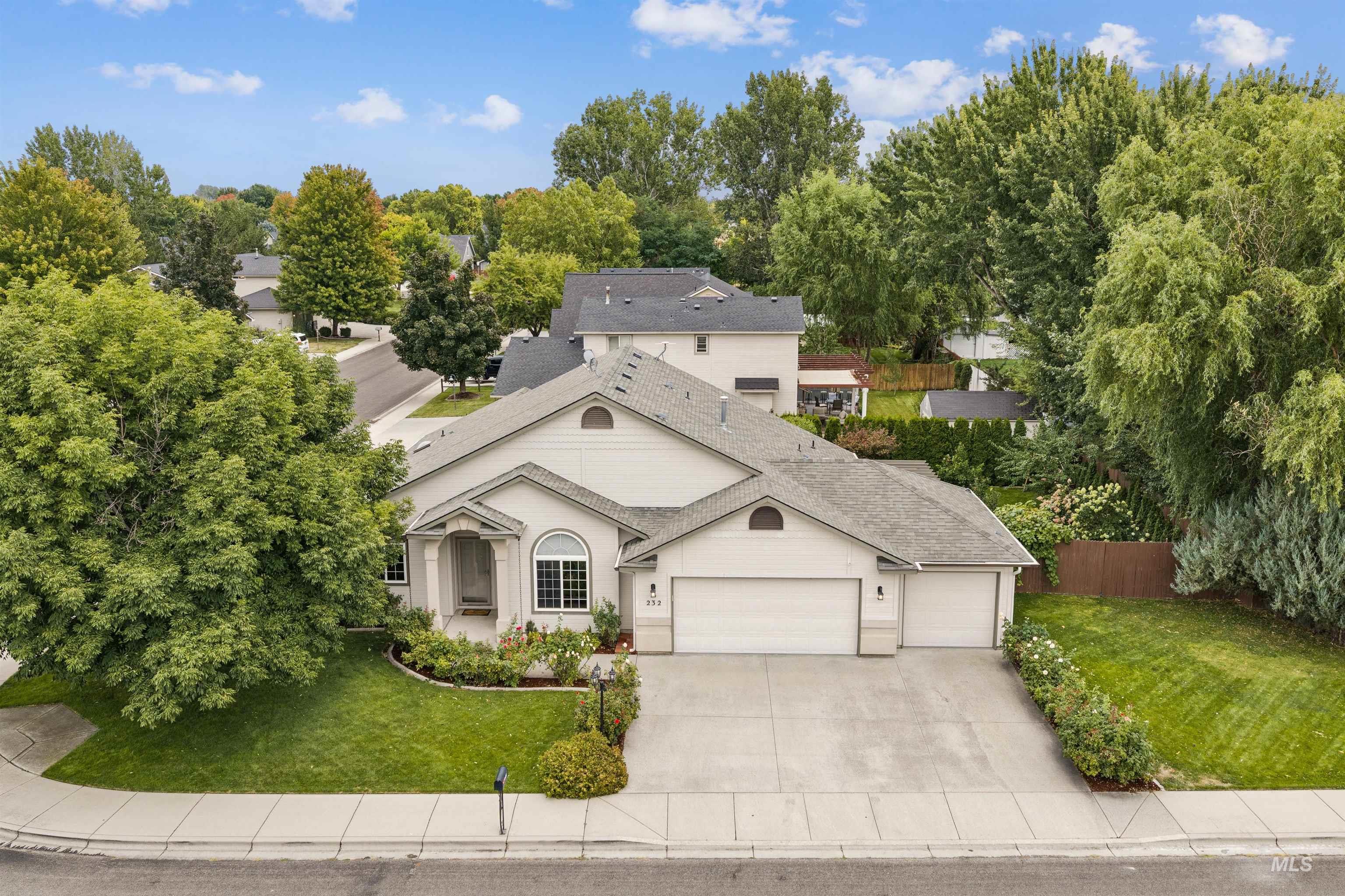 Aerial view of a light-colored home with a two-car garage, broad driveway, and landscaped front yard.
