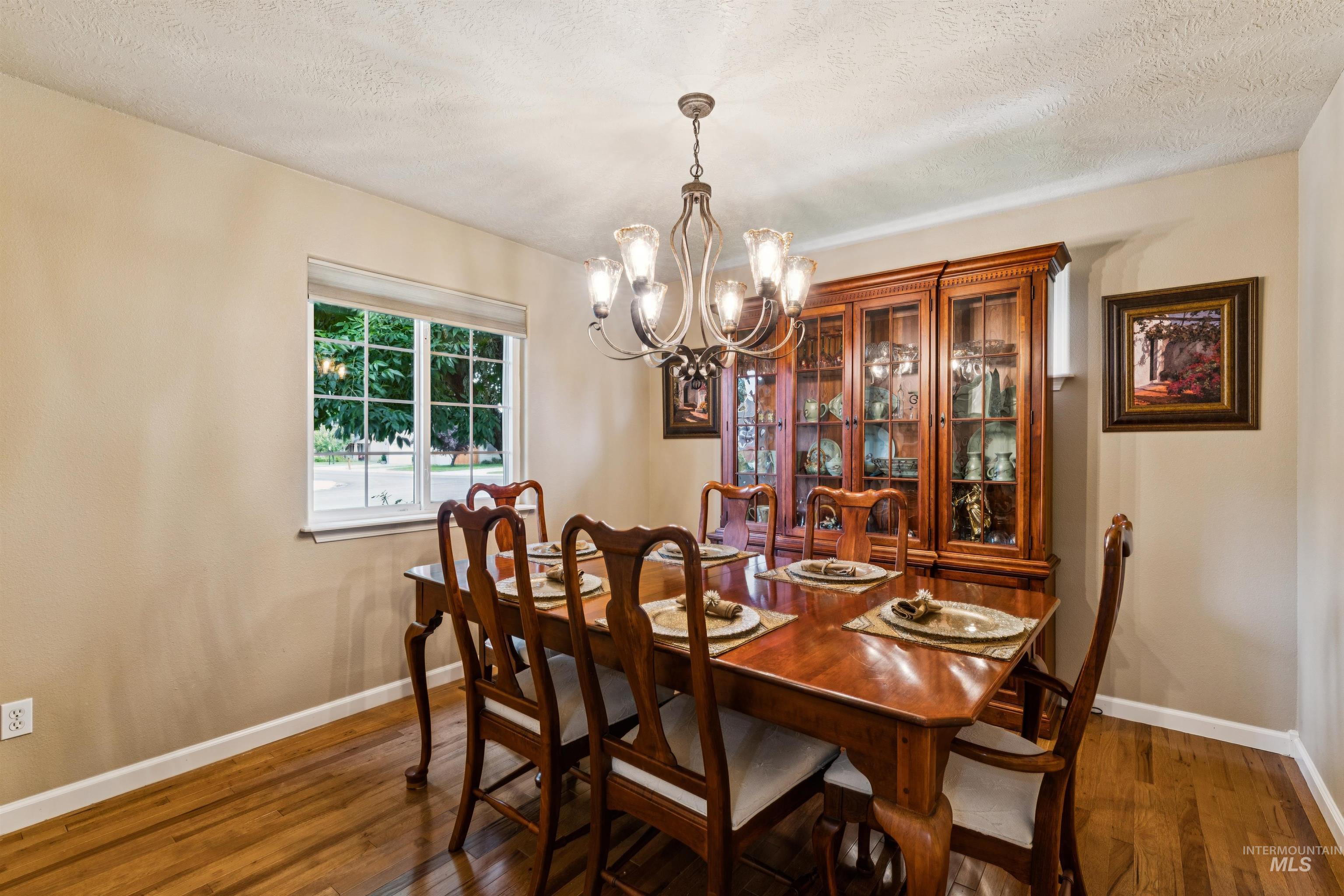 Dining room with a set wooden table, glass-front china cabinet, chandelier, and hardwood floors.