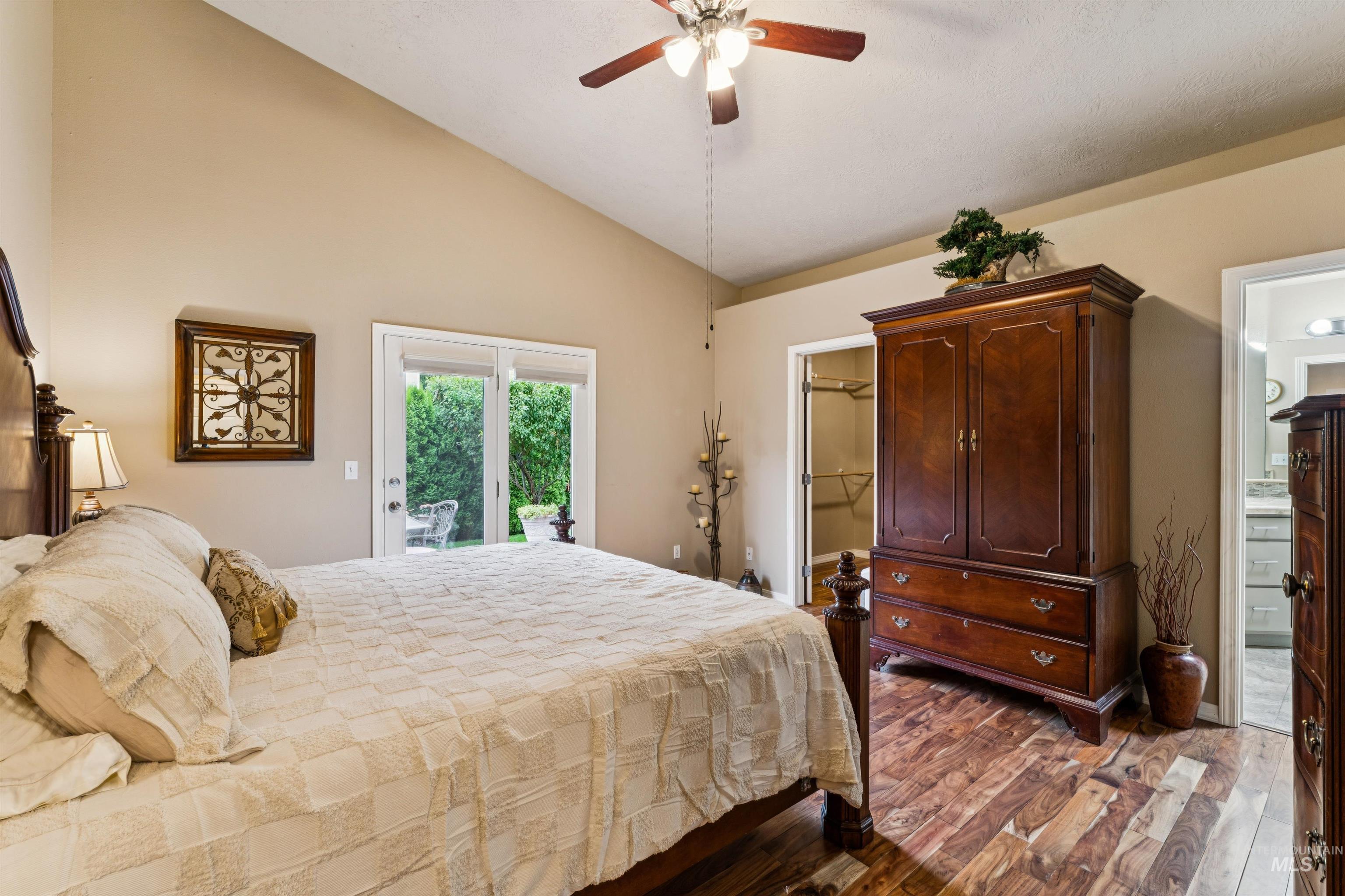 Furnished bedroom with a large bed, dark wood armoire, and sliding glass door to greenery.