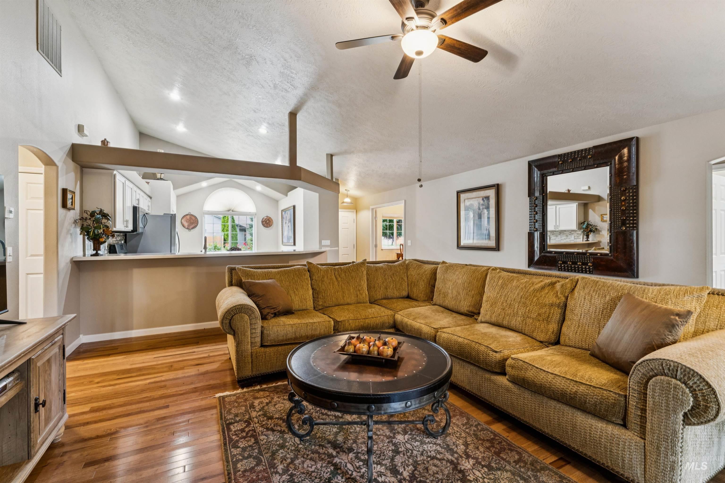 Living room with a brown sectional, hardwood floors, vaulted ceiling, and open kitchen.