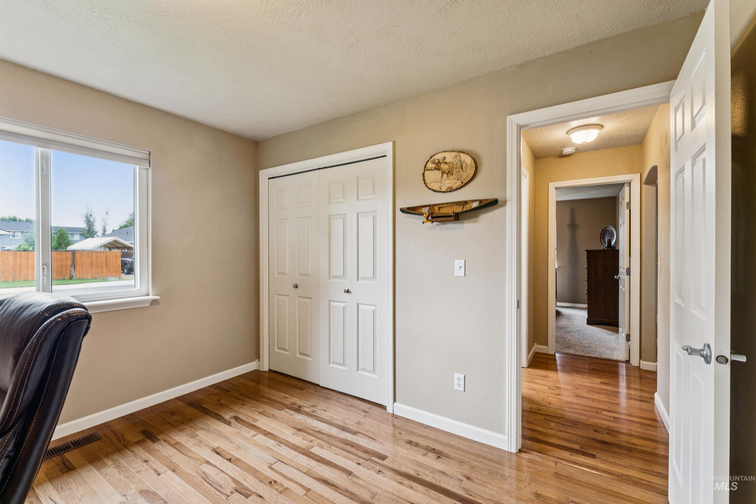 Bedroom with hardwood floors, double closet doors, and a large window overlooking the yard.