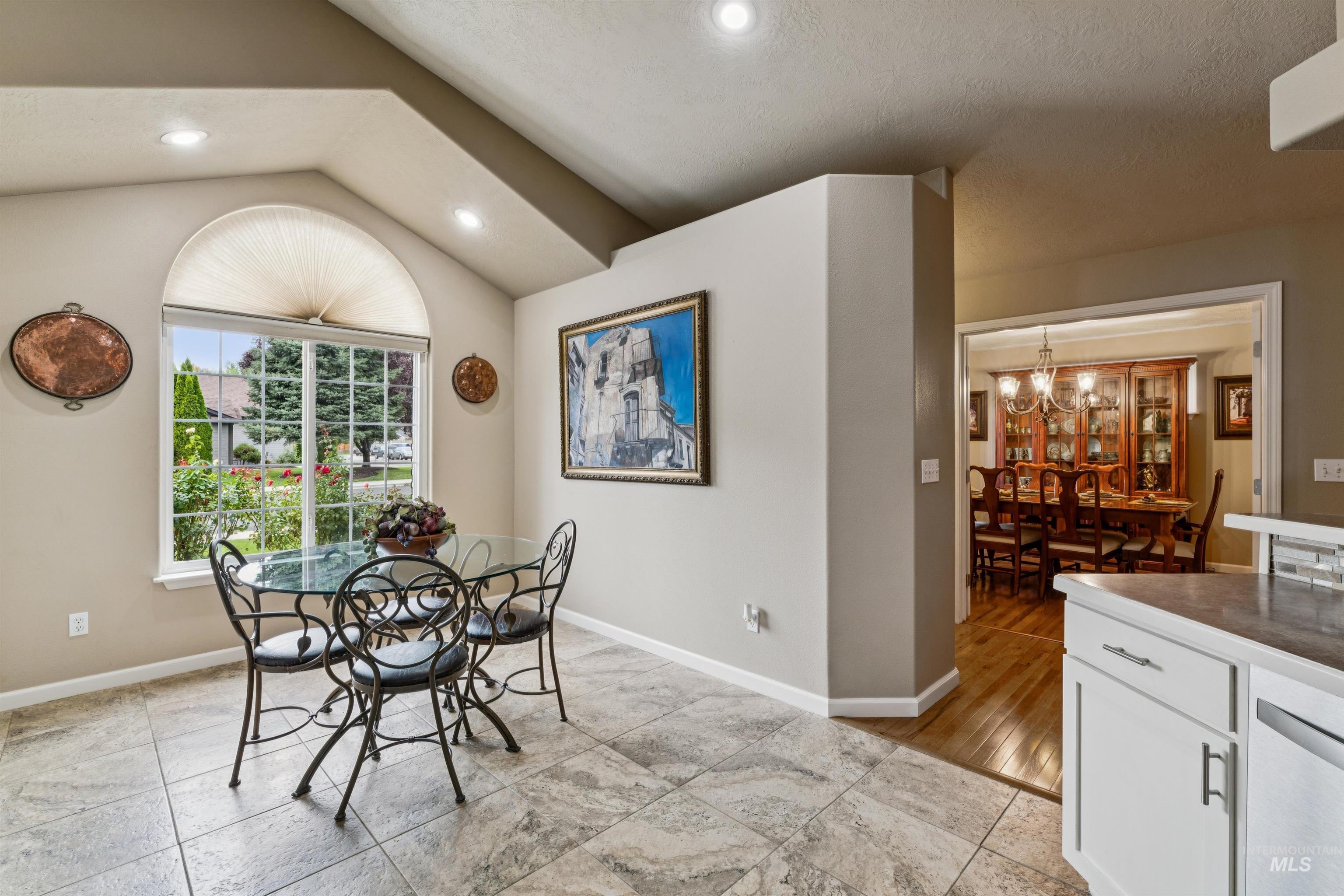 Dining nook with a glass table beside an arched window, opening to a formal dining room.