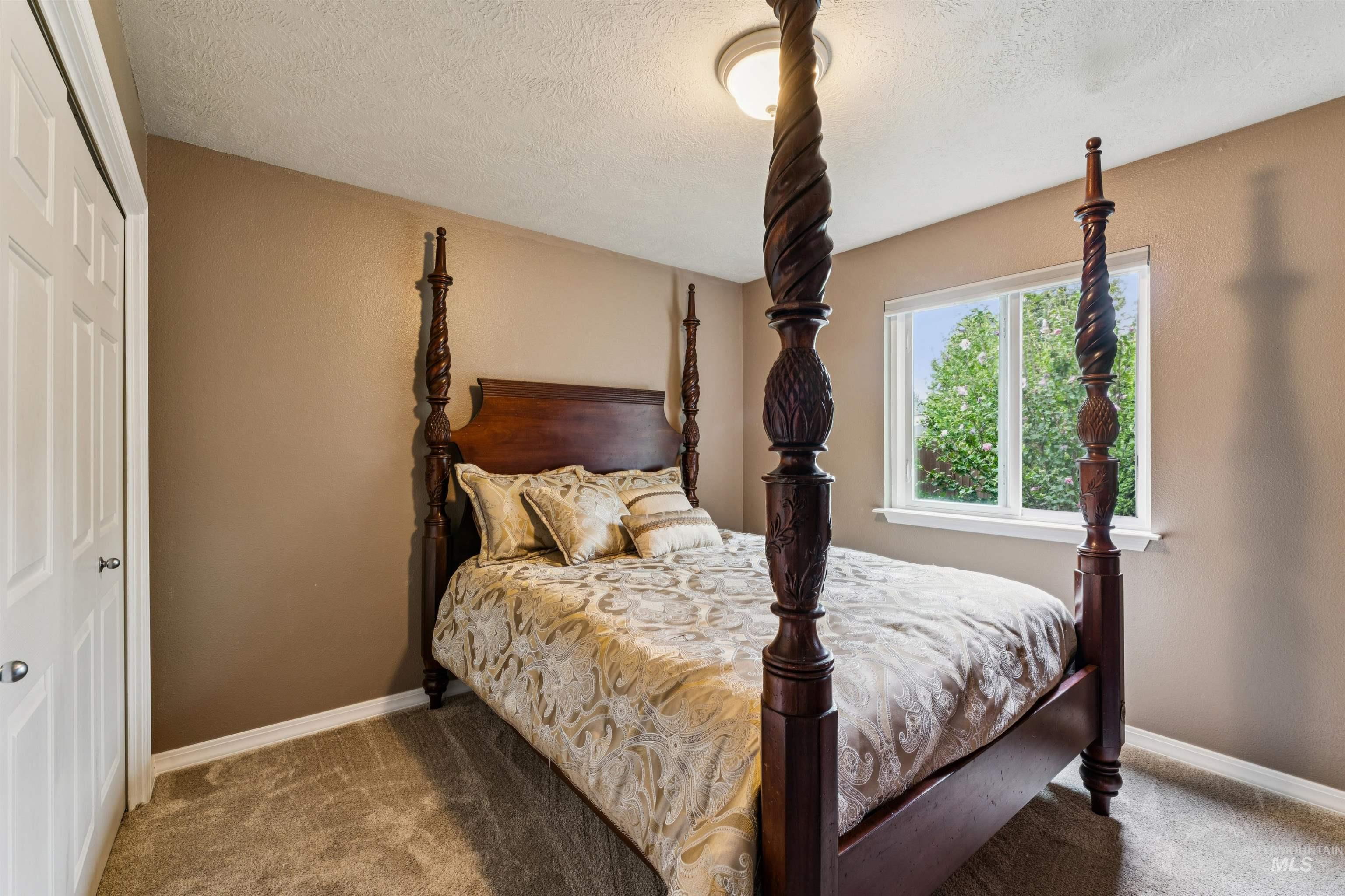 Bedroom with a carved four-poster bed and patterned bedding beside a window overlooking greenery.