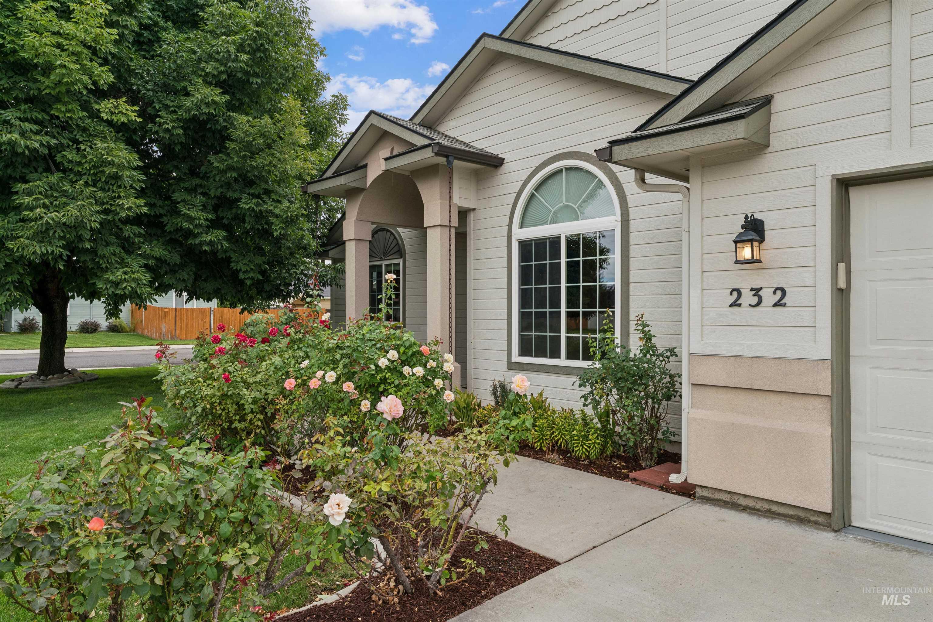House entrance with arched window and rose-filled garden beside the garage.